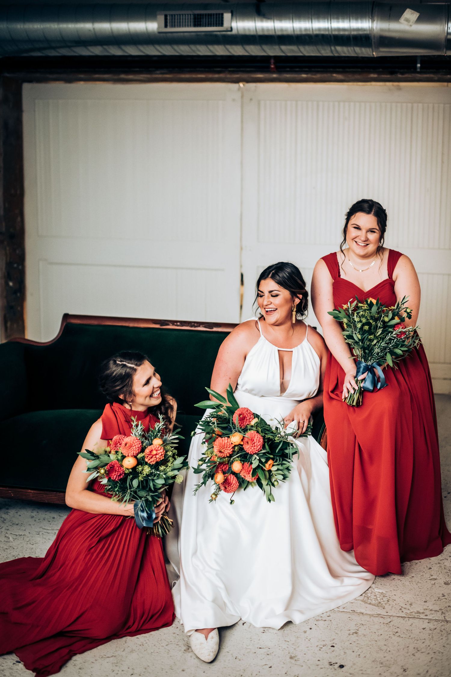Wedding party members in red dresses and white gown posing with floral bouquets.