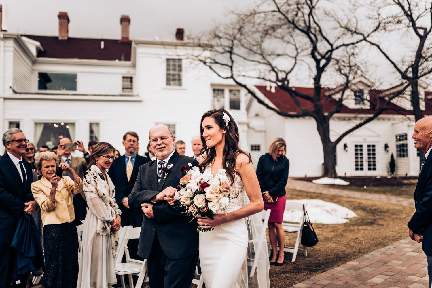 Wedding ceremony in progress outside historic white building with red roof.