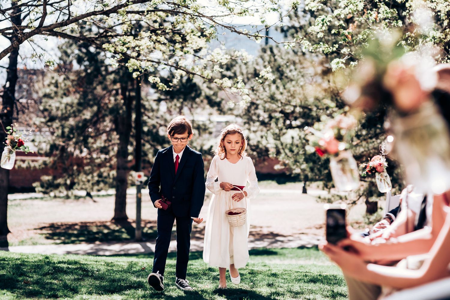 Outdoor springtime wedding procession with blooming trees creating a romantic backdrop.
