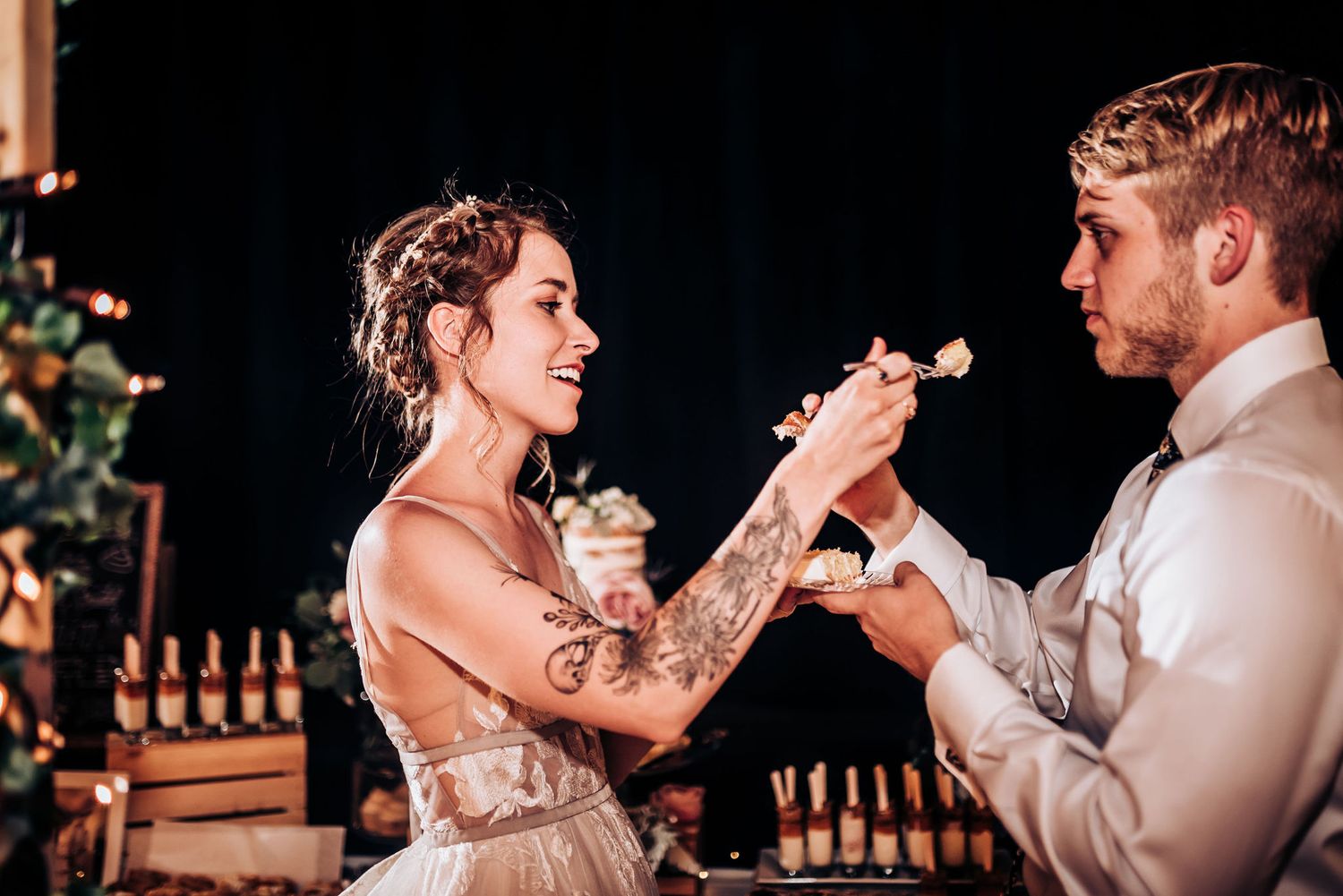 Wedding couple laughs while feeding each other cake during their reception celebration.