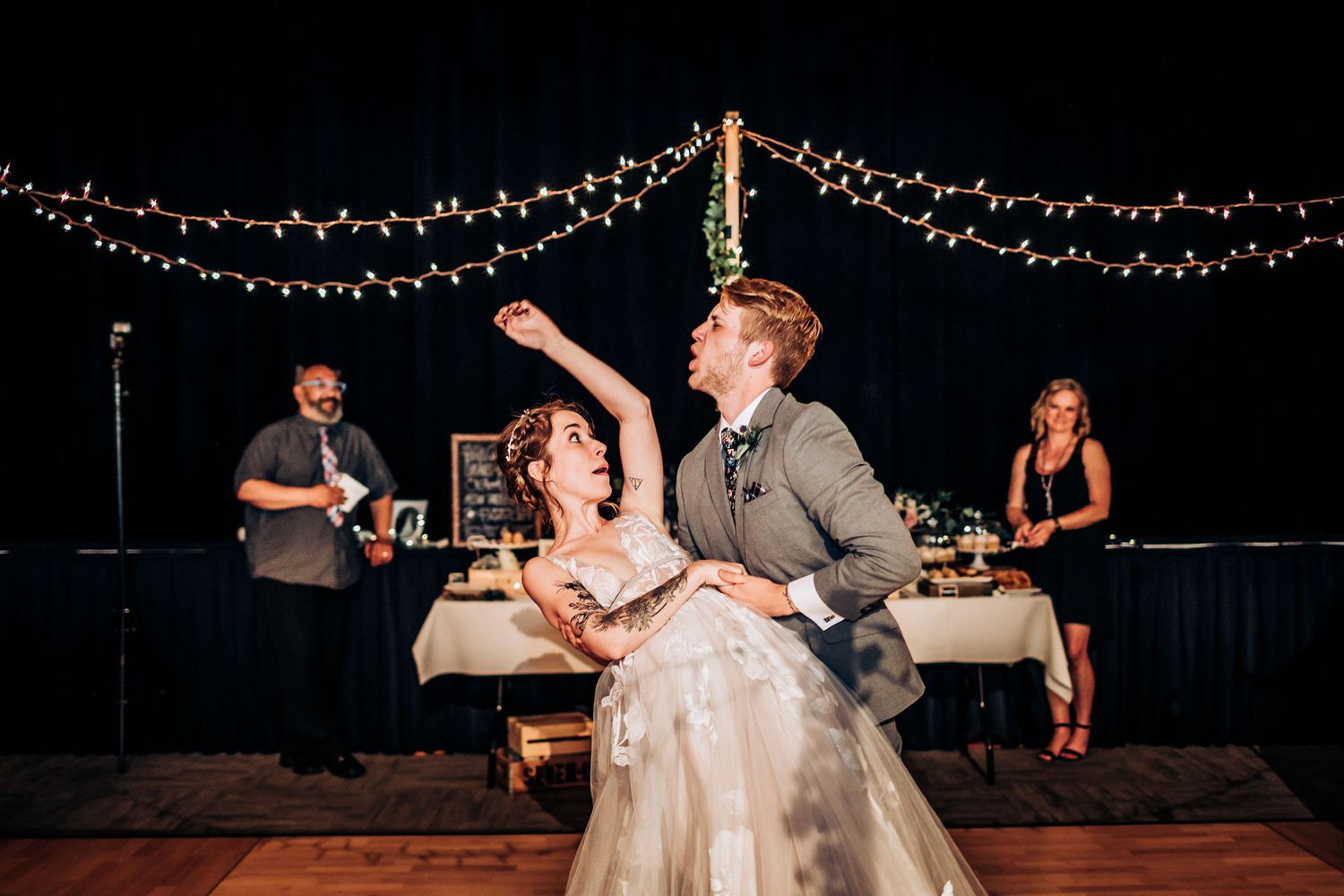 Newlyweds perform a playful dance move during their reception under festive string lights.