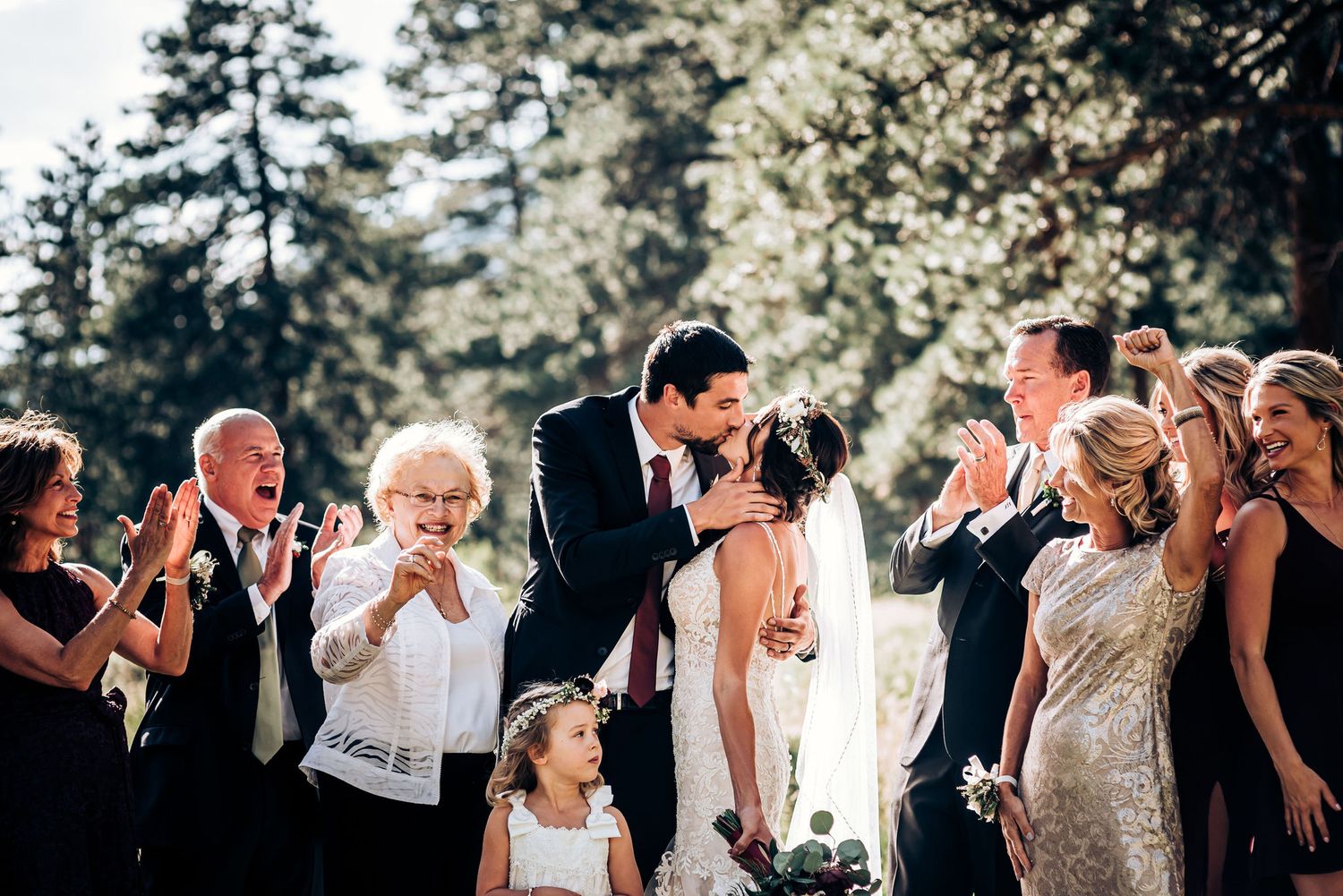 Wedding guests react with joy during an outdoor ceremony as the couple shares their first kiss.