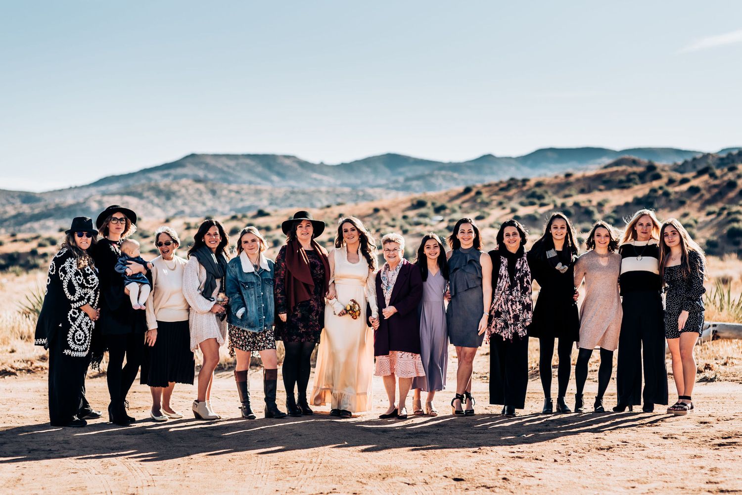 Group photo of wedding attendees standing together in the desert with mountains in background.