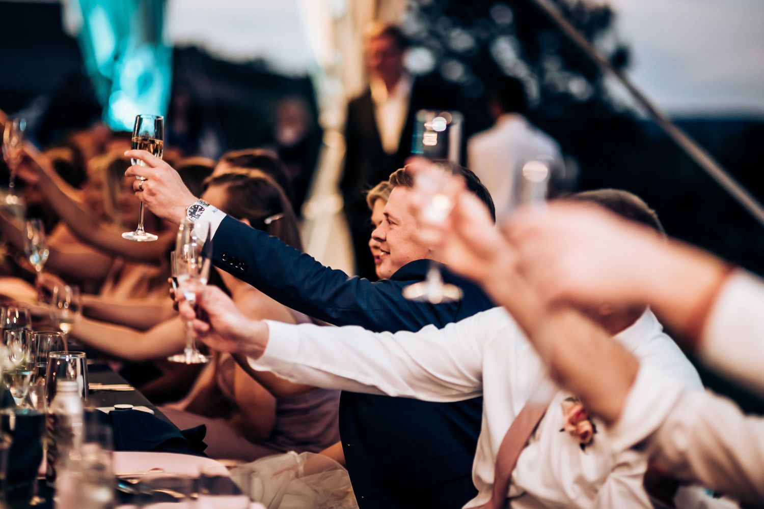 Wedding guests raising glasses for a toast during outdoor reception.