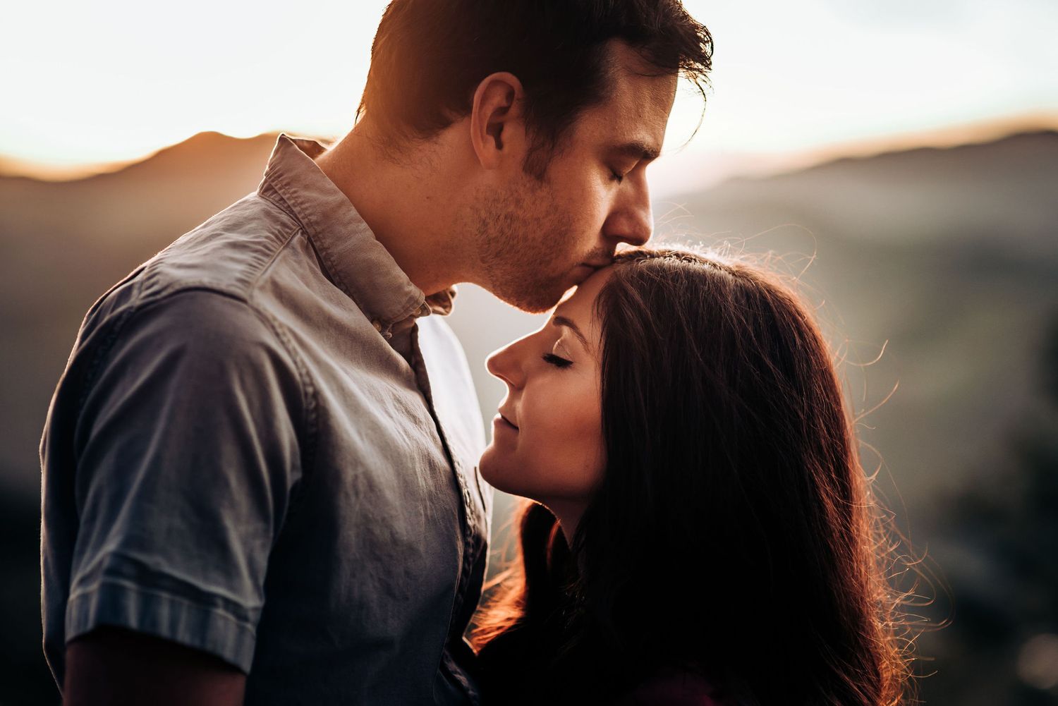 Tender moment between couple against mountain landscape at sunset.
