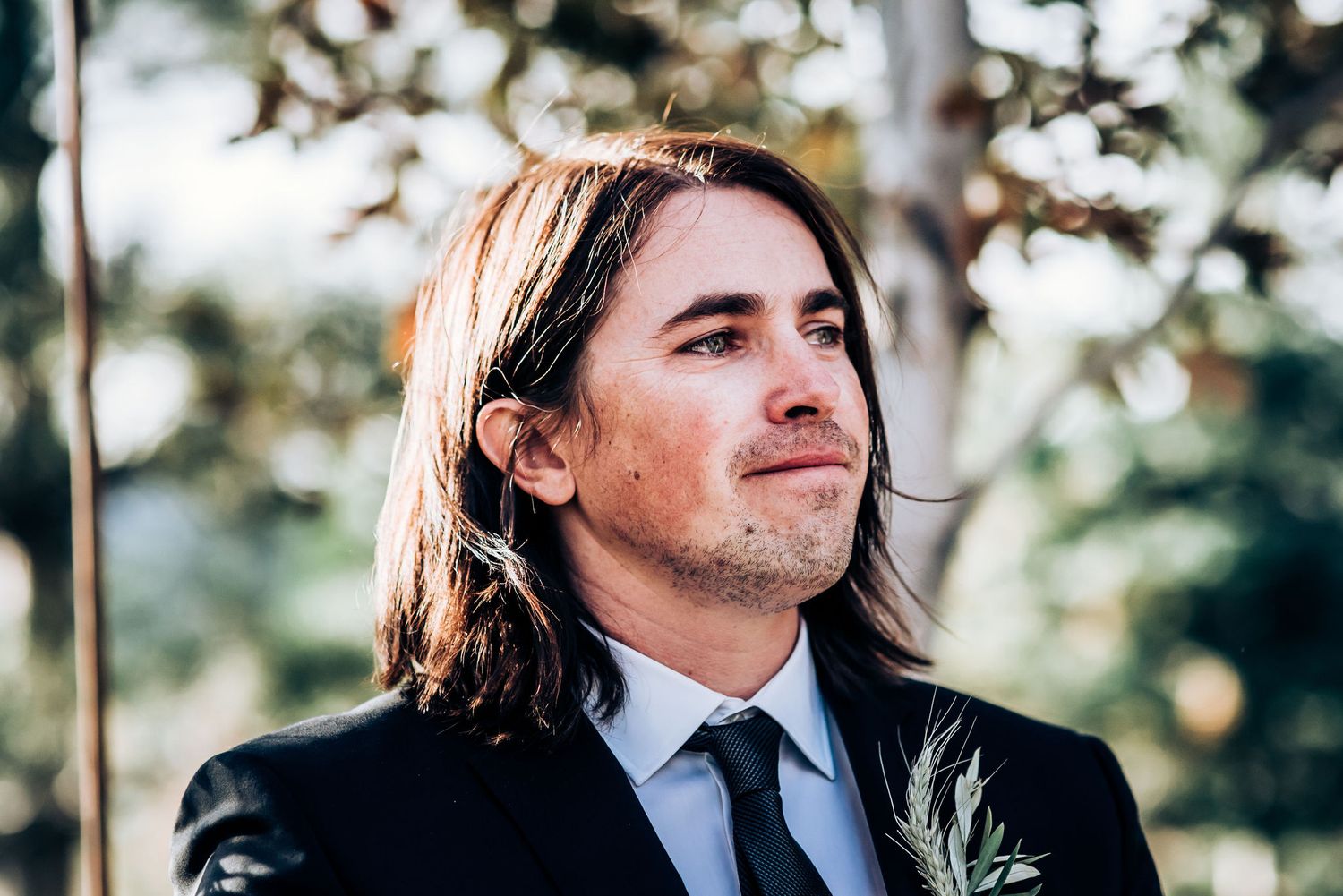 Black-suited figure with long hair stands outdoors during autumn wedding ceremony.