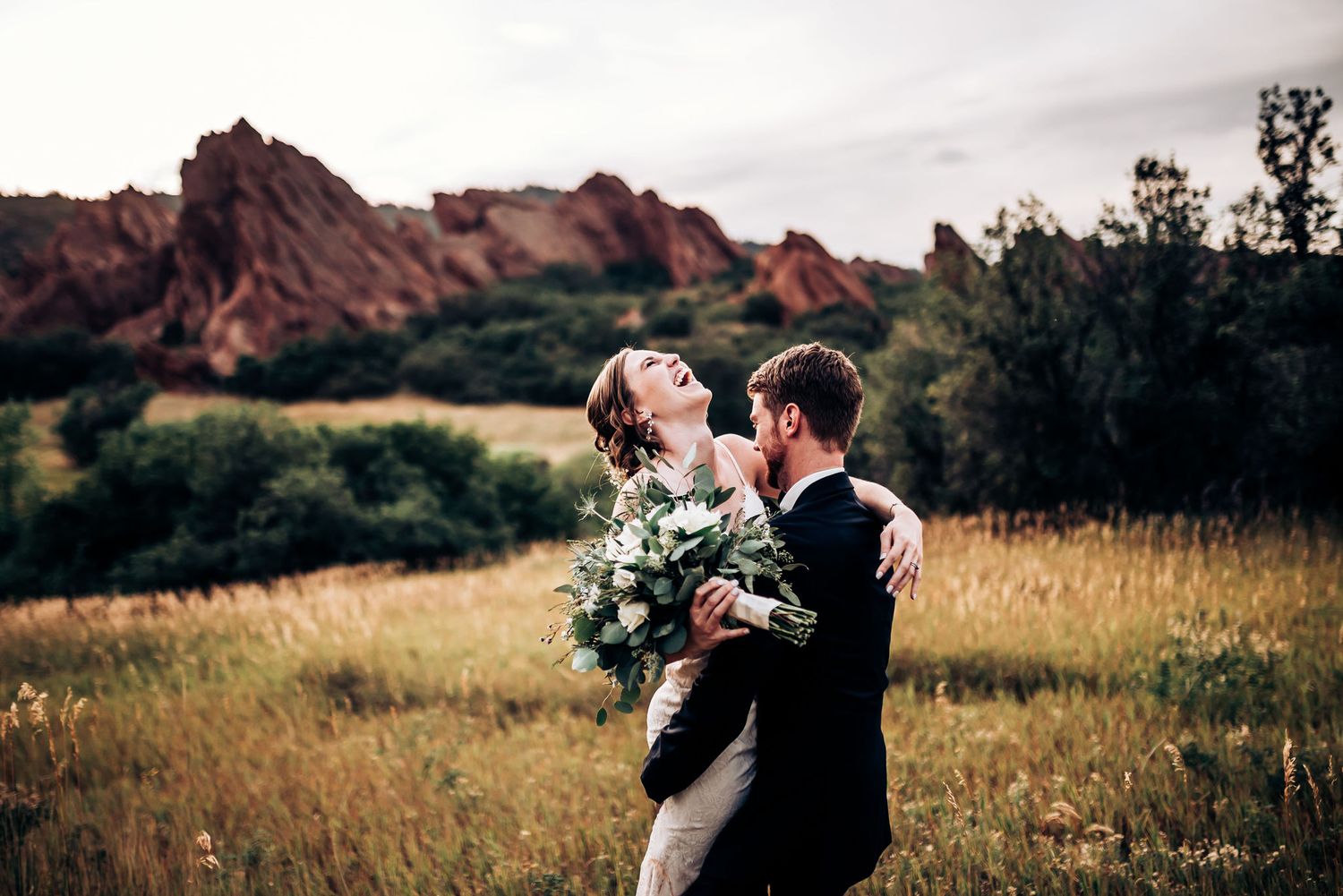 Newlyweds celebrate with bouquet against dramatic mountain landscape.