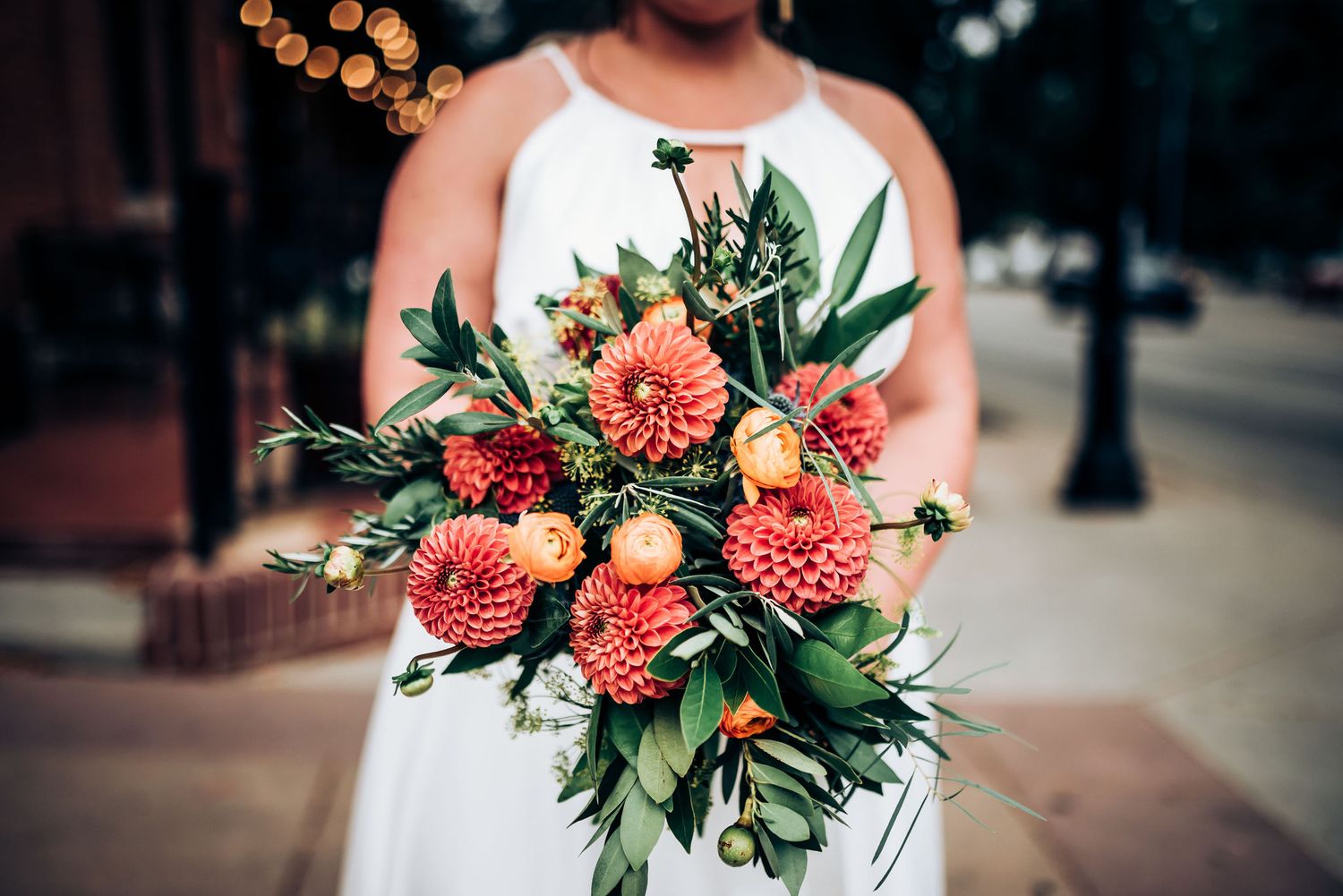 Stunning coral dahlia bridal bouquet with mixed florals captured in urban setting.