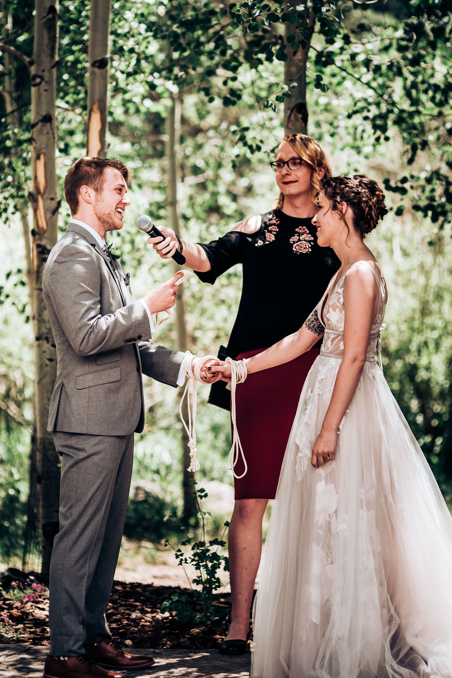 Outdoor wedding ceremony with officiant and couple during vow exchange in wooded setting.