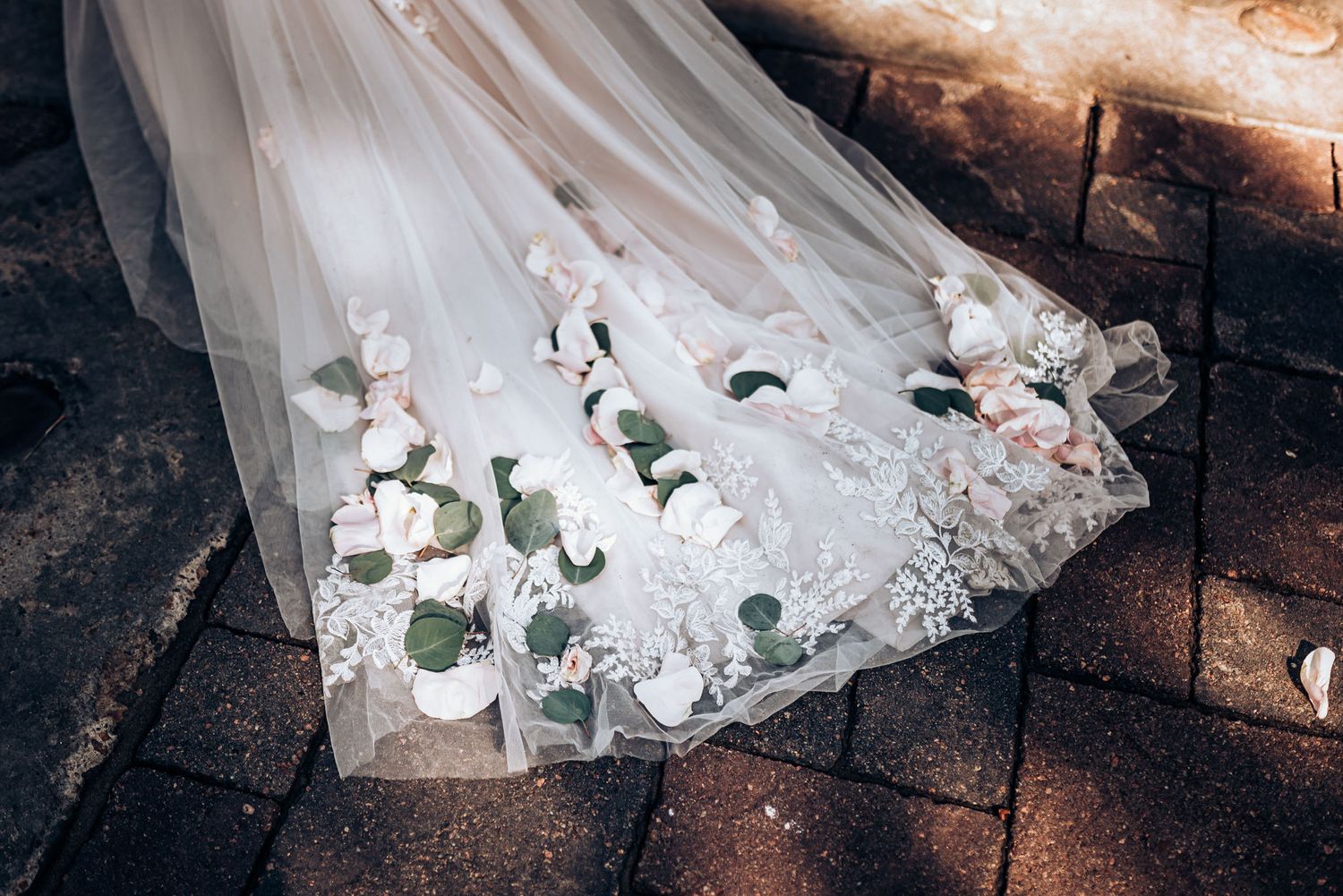 A wedding dress train decorated with delicate roses and lace lies on stone pavement.