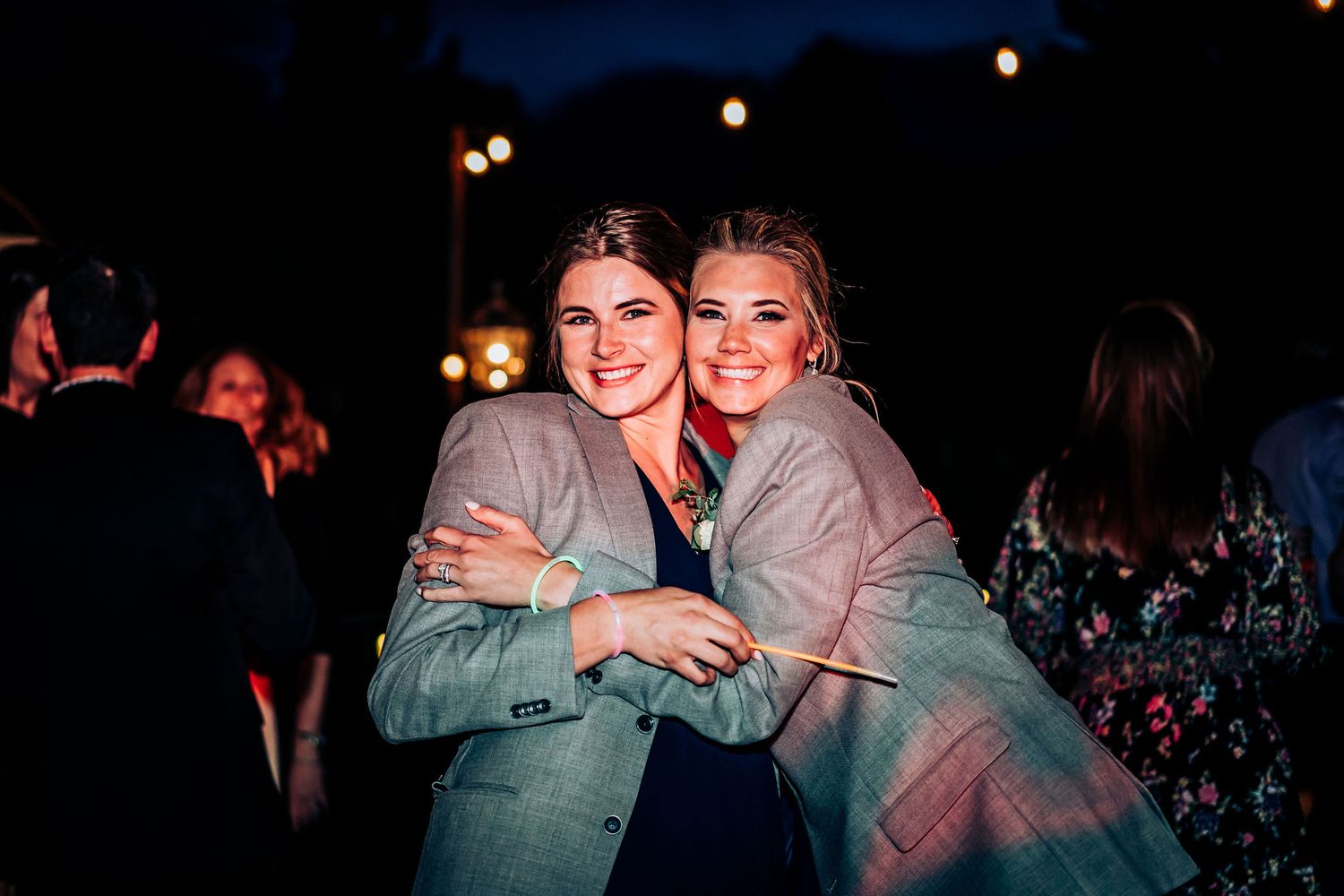 A nighttime celebration with guests embracing under outdoor lighting.