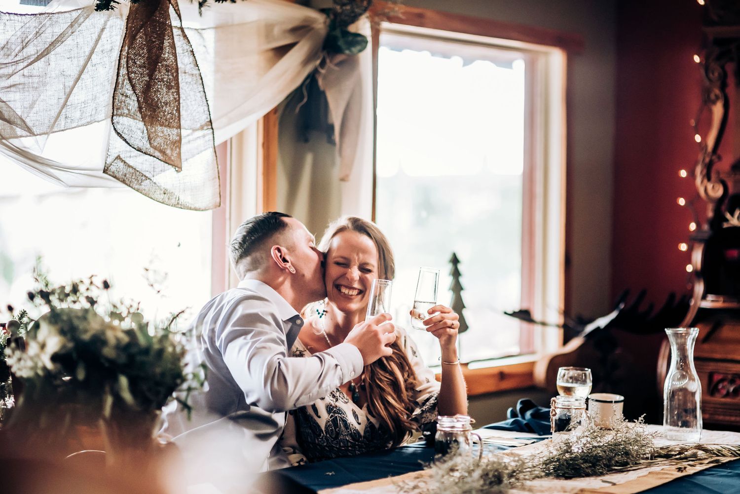 A joyful moment shared during a reception with window light streaming into the rustic venue.