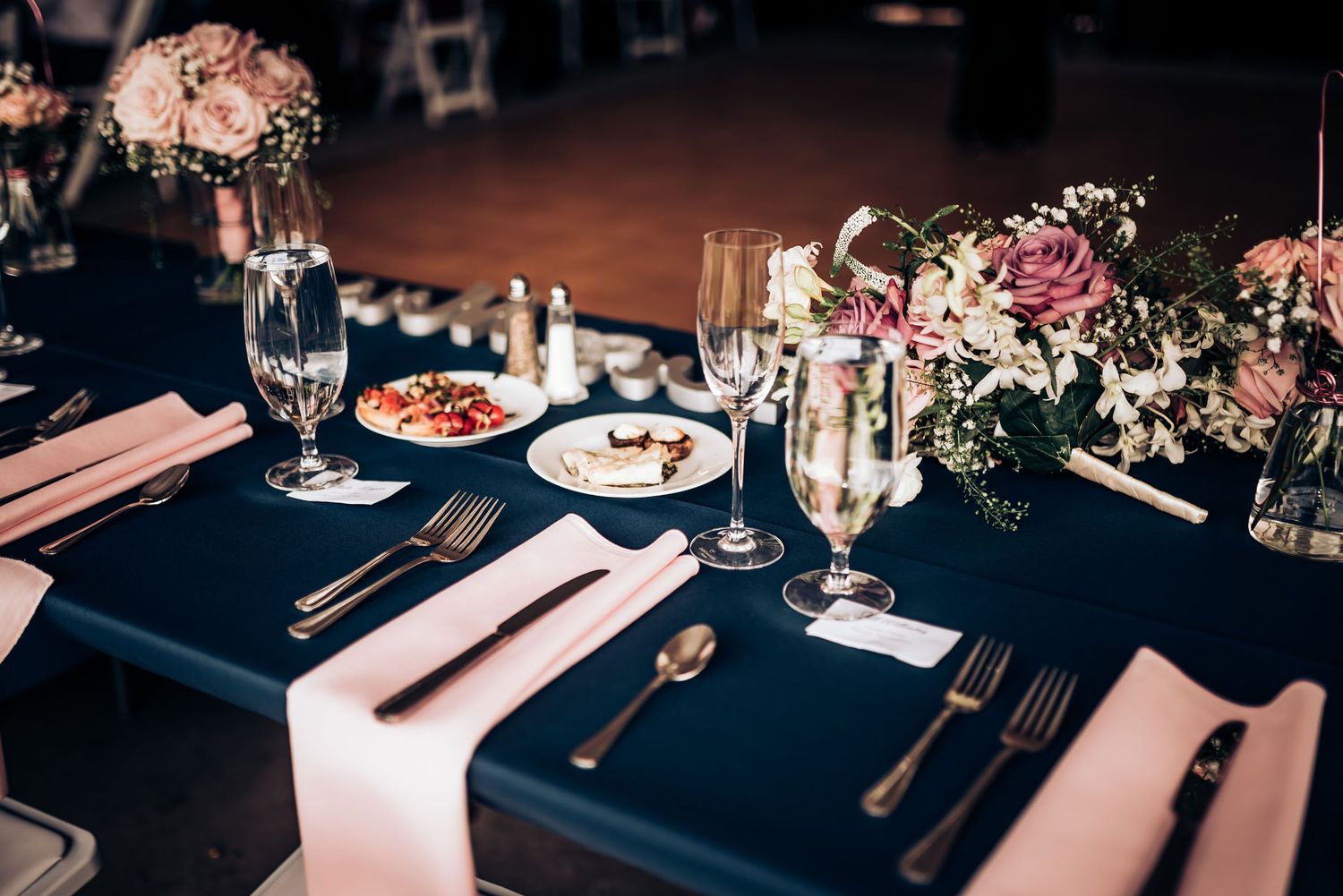 Navy and pink wedding table setting with floral centerpieces and formal place settings.