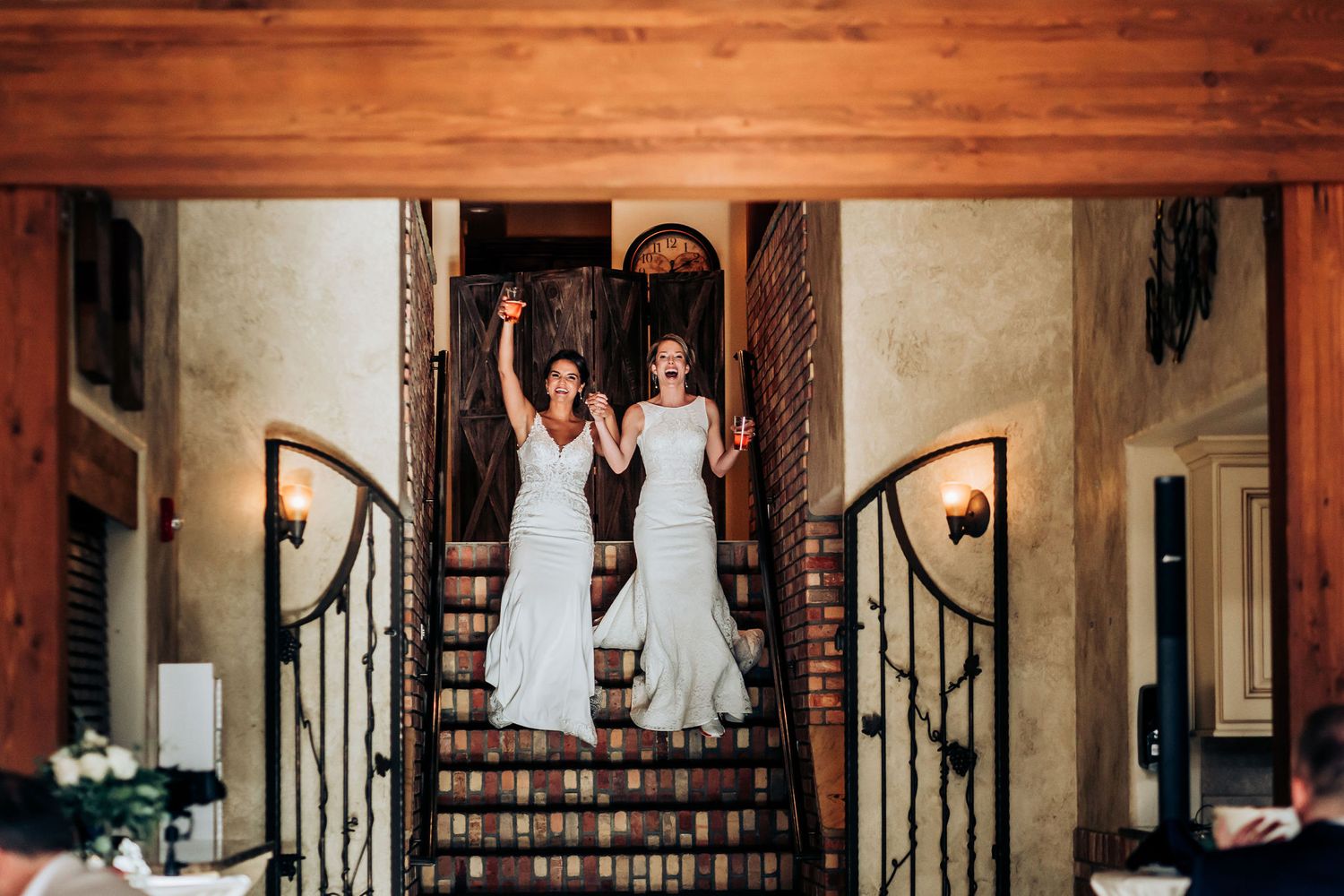 Two wedding dresses jumping in synchronization on elegant wooden staircase.