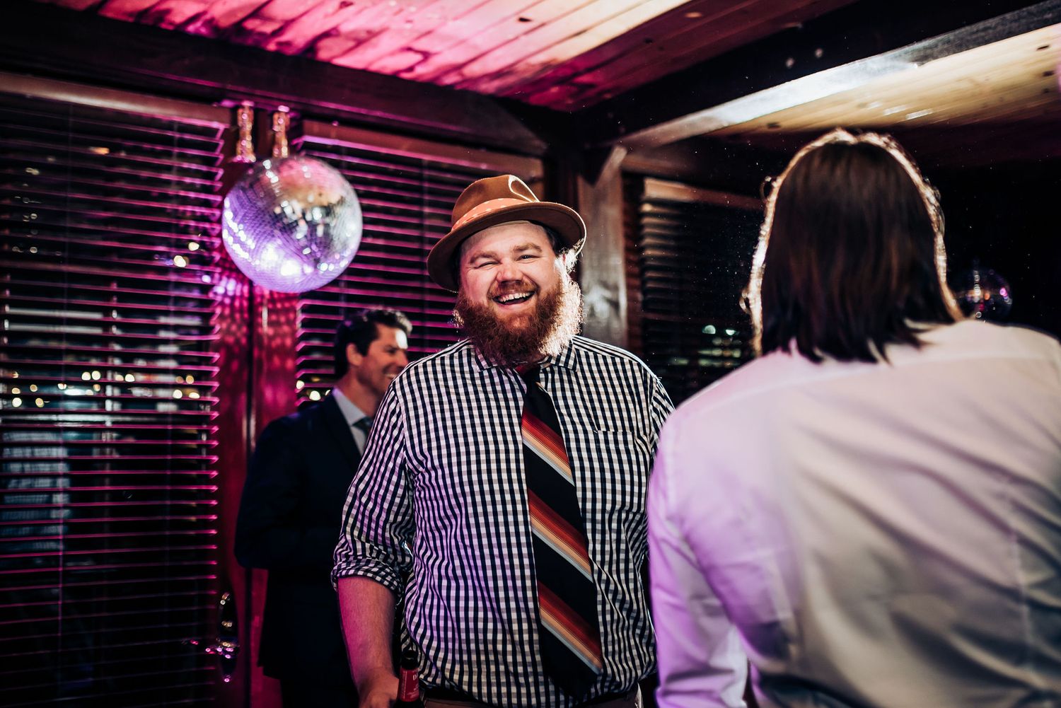 Partygoers enjoying conversation under purple lighting with a disco ball overhead.