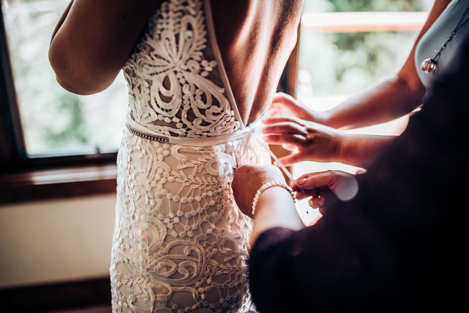Close-up detail shot of intricate lace wedding dress being buttoned up.
