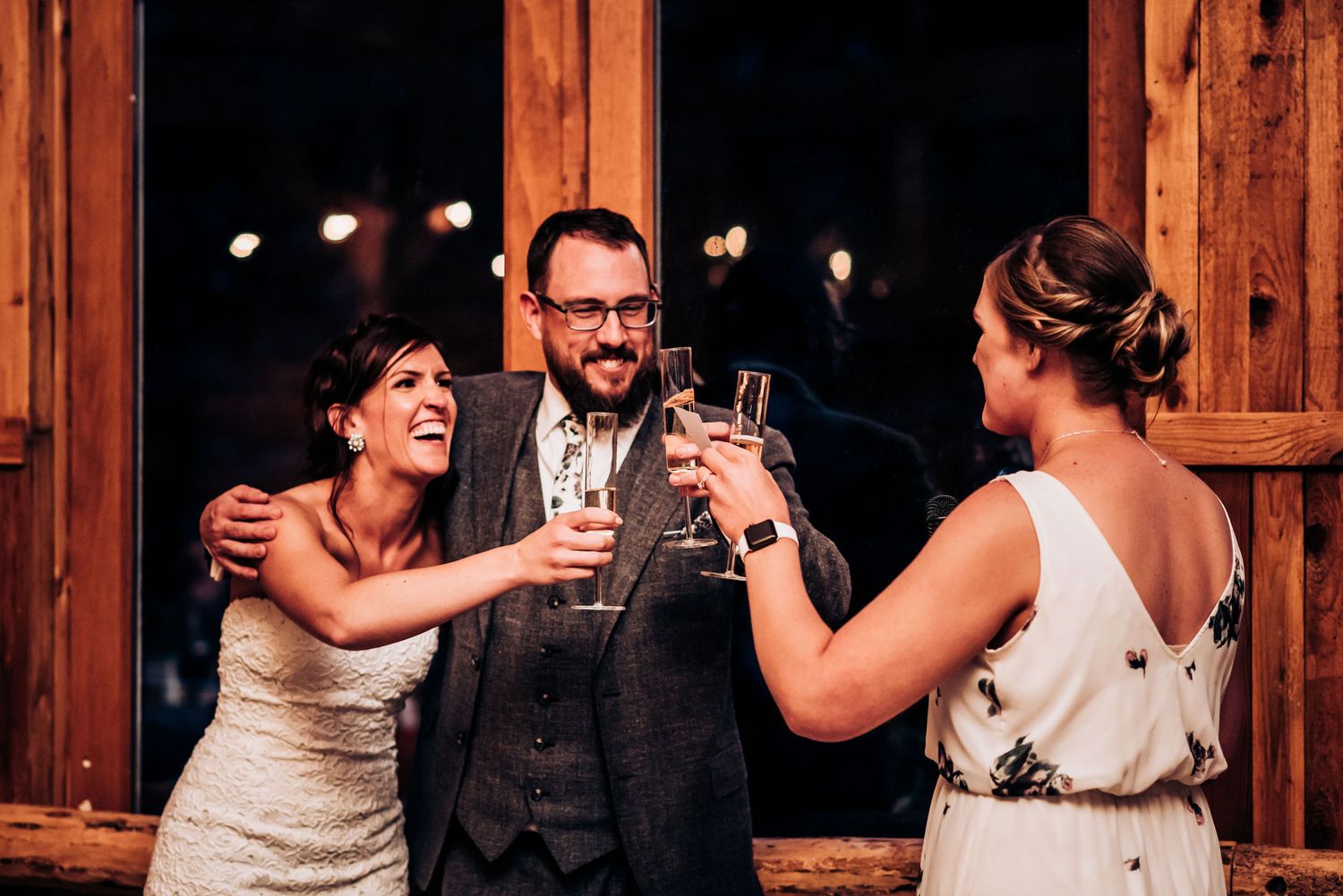 Celebratory toast moment at evening wedding reception in wooden lodge venue.