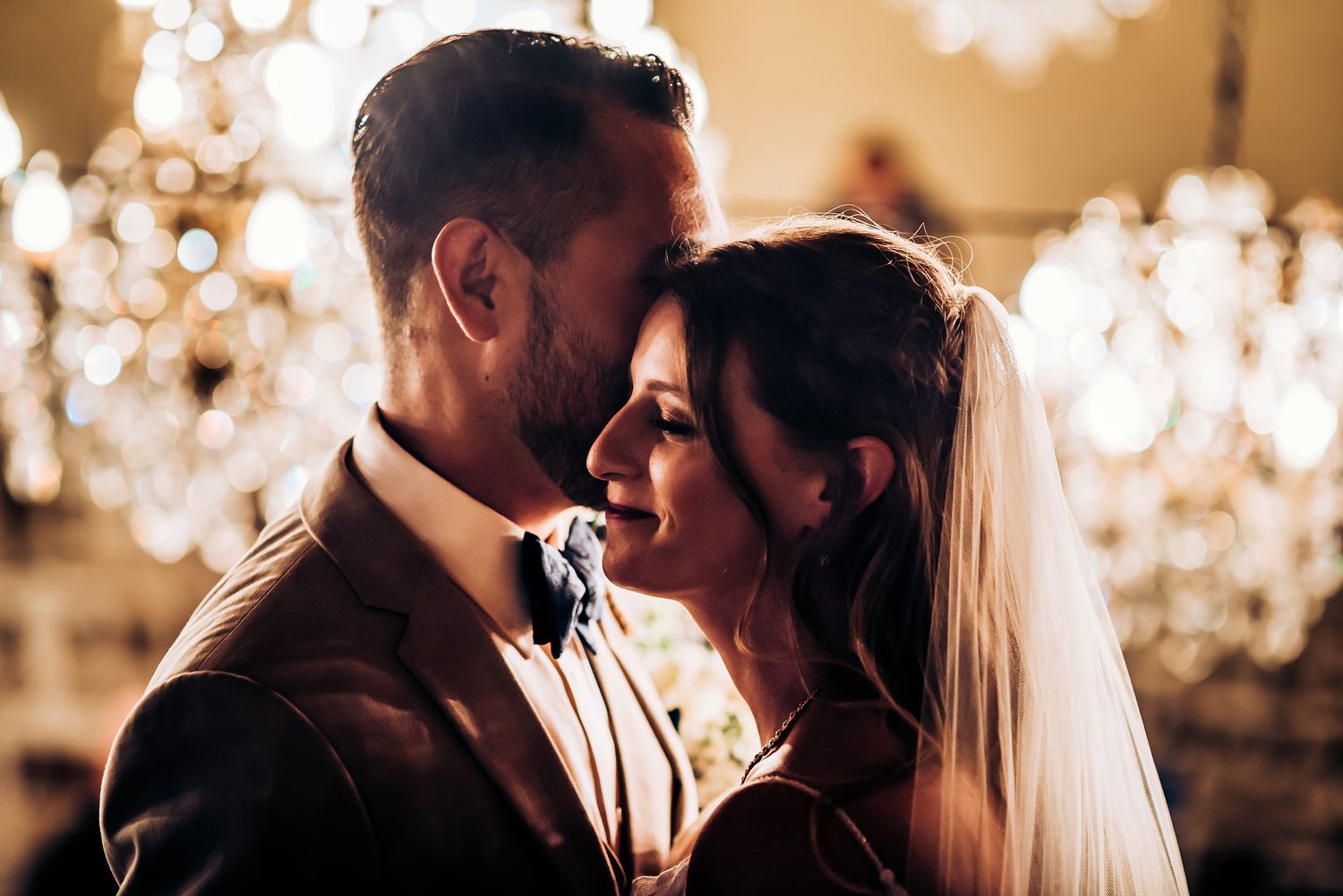 Intimate wedding portrait with sparkling chandelier lights creating romantic bokeh effect.
