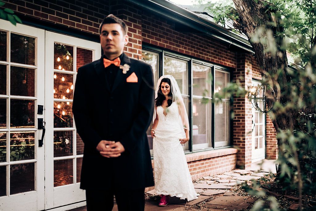 A wedding couple positioned for their first look outside a brick building.