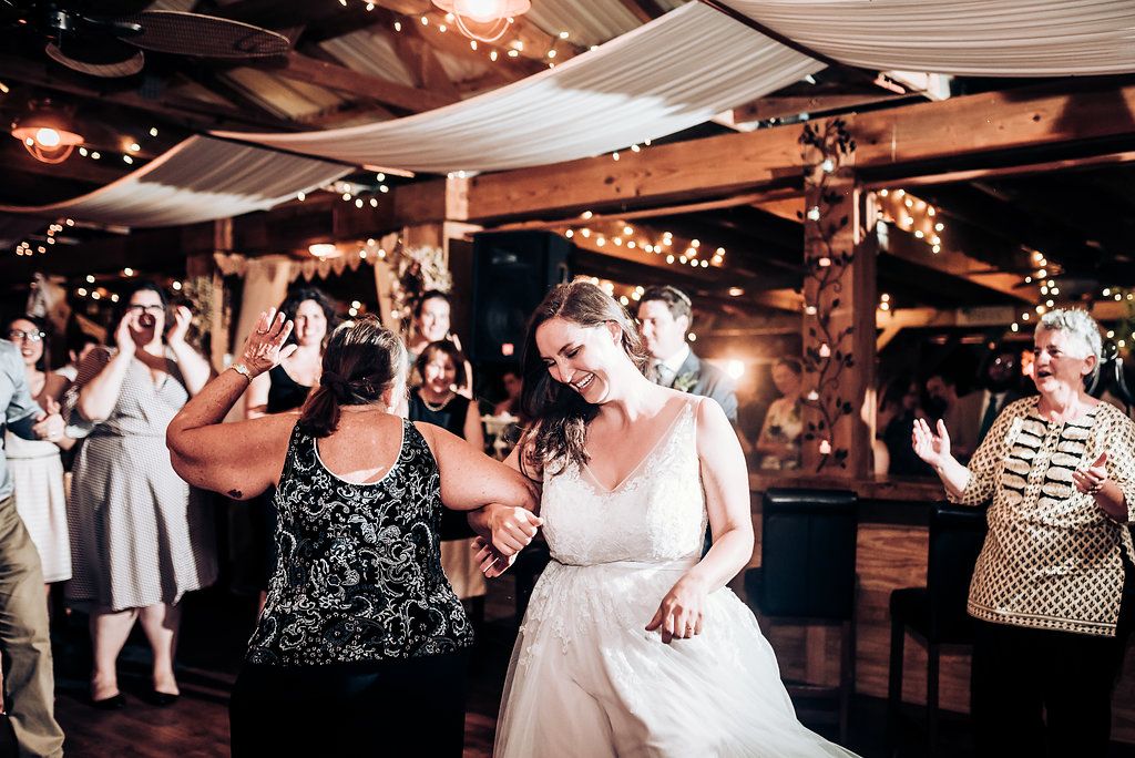 Wedding guests dance together on a dimly lit dance floor decorated with string lights at a reception celebration.