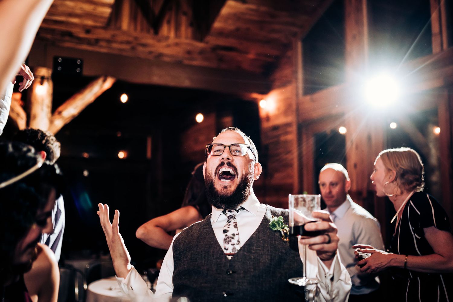 Enthusiastic guest celebrating with raised arms at rustic indoor reception.
