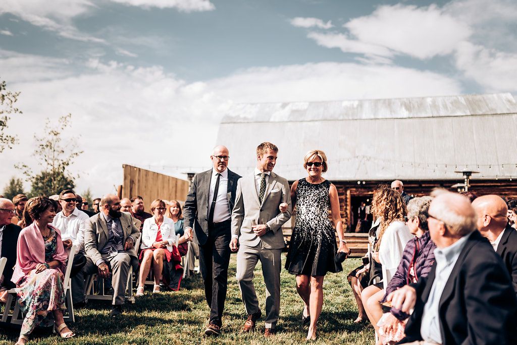 Outdoor wedding ceremony with guests seated on lawn in front of rustic barn.