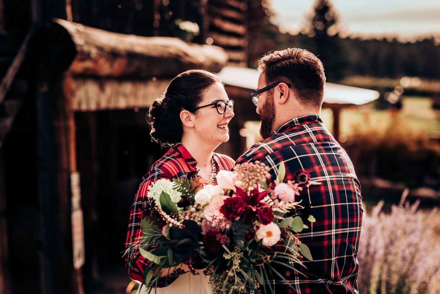 A couple shares a sweet moment outdoors with a stunning floral bouquet in burgundy and pink.