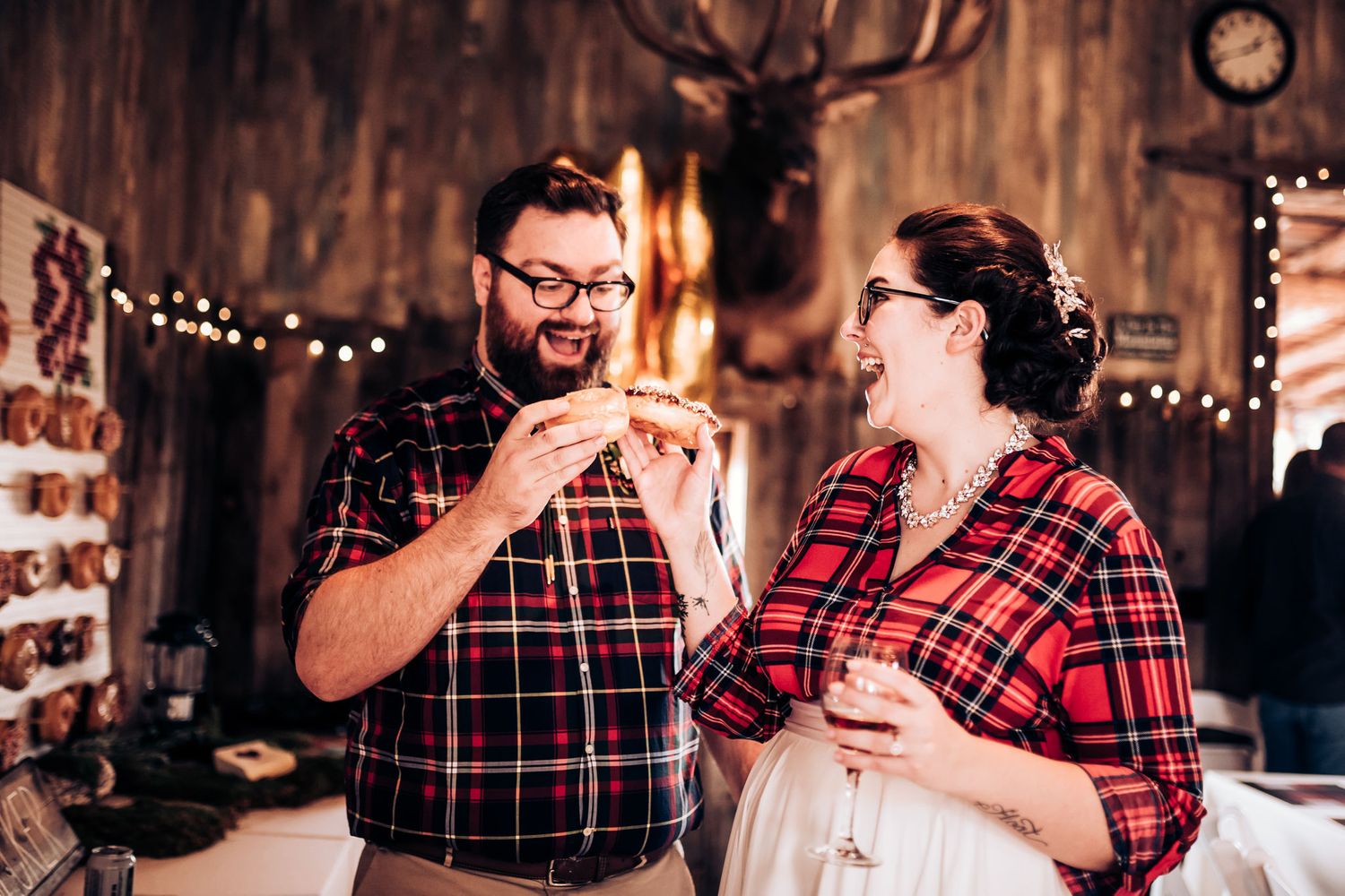 A couple in coordinated plaid shirts having fun with snacks in a rustic cabin setting.