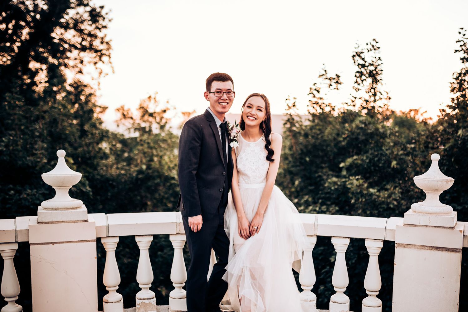 Wedding couple standing on elegant white balustrade terrace at sunset.