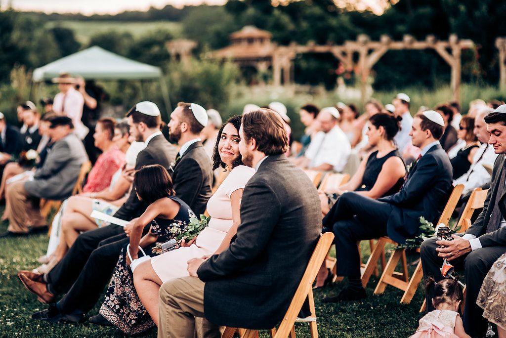 Wedding guests seated on wooden folding chairs at outdoor ceremony venue.