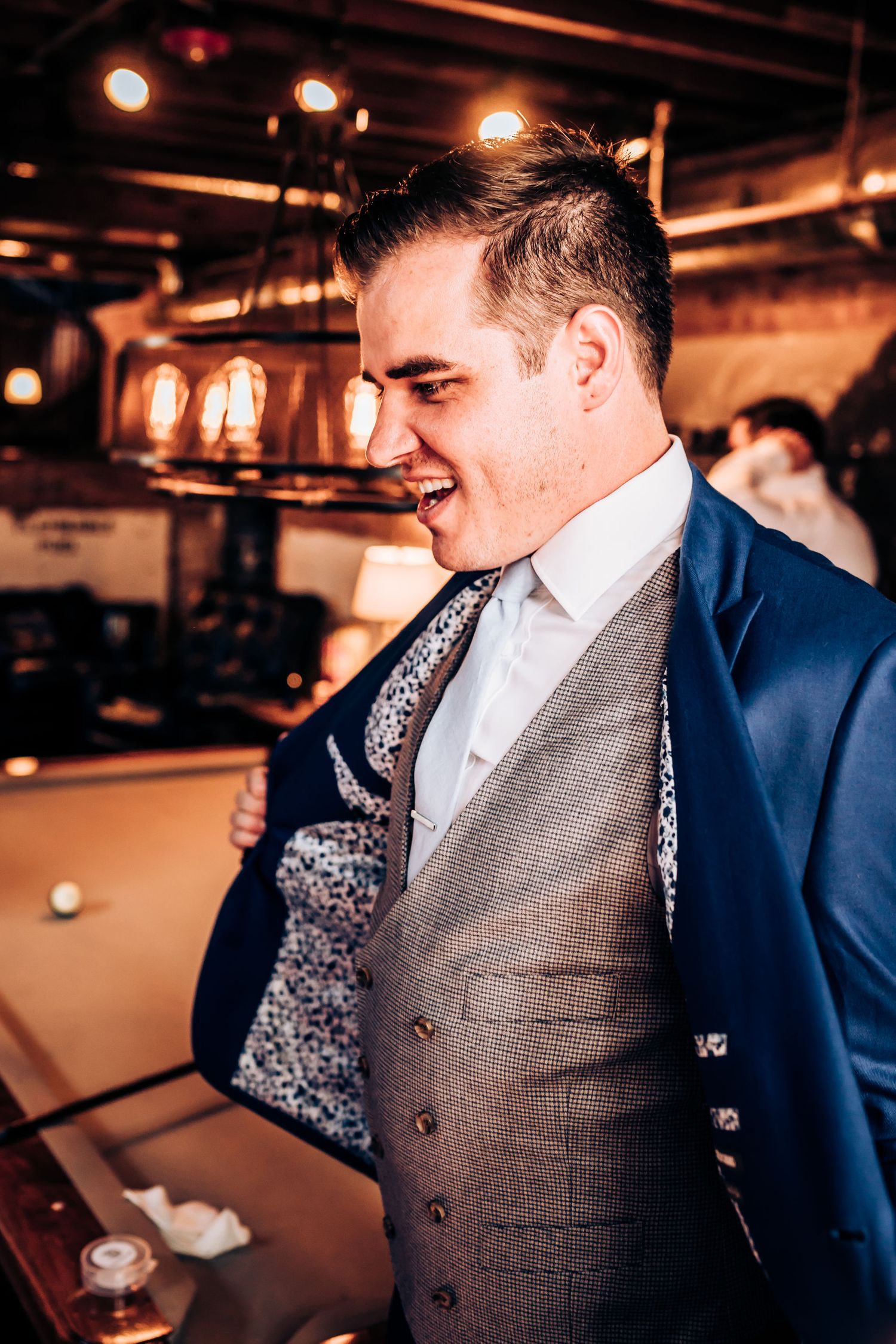 Person in formal vest and blazer smiling in warm indoor lighting.