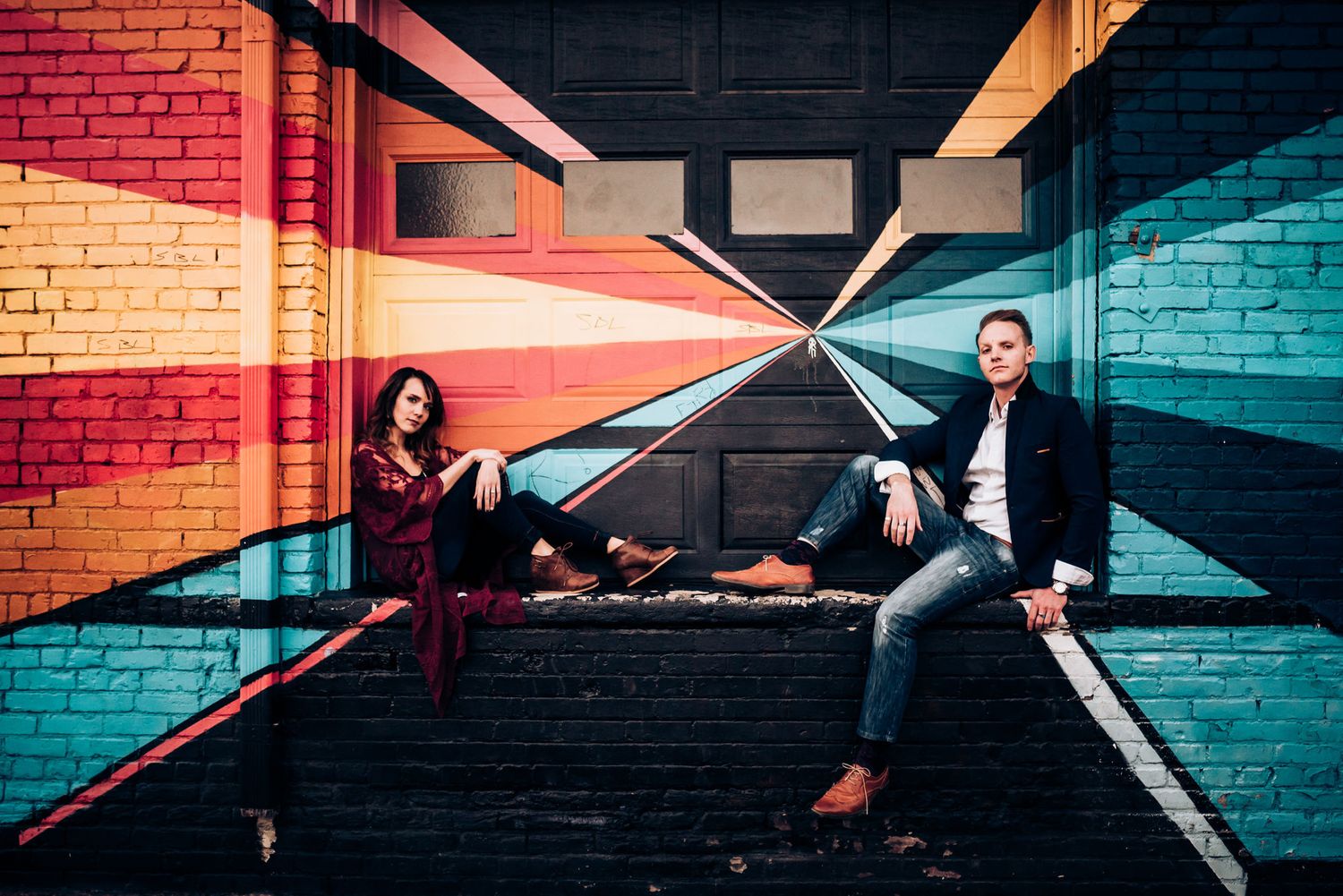 Two people sitting casually in modern hallway with striking geometric wall patterns.