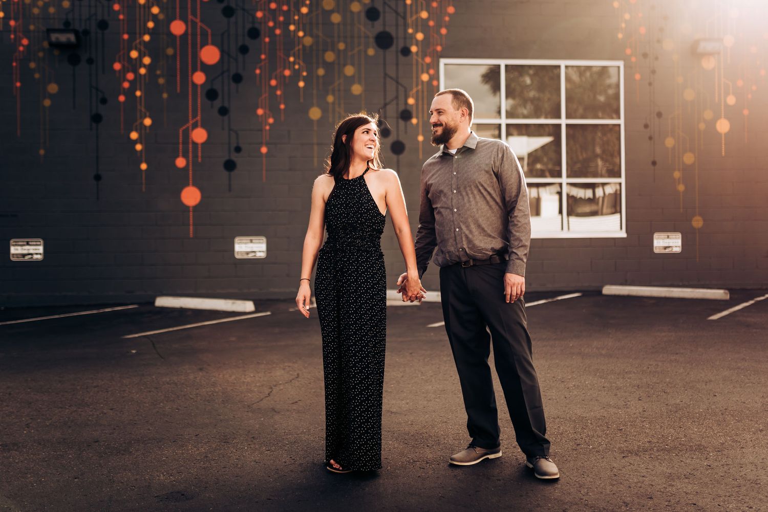 Couple in formal attire poses against wall with glowing orange lights.