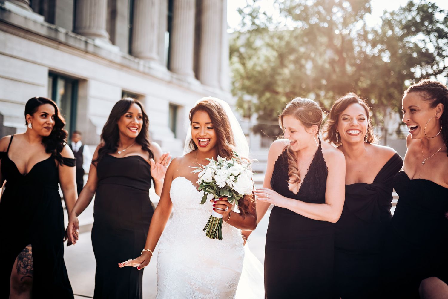 Joyful wedding party celebrating and laughing together outside building with classic columns.