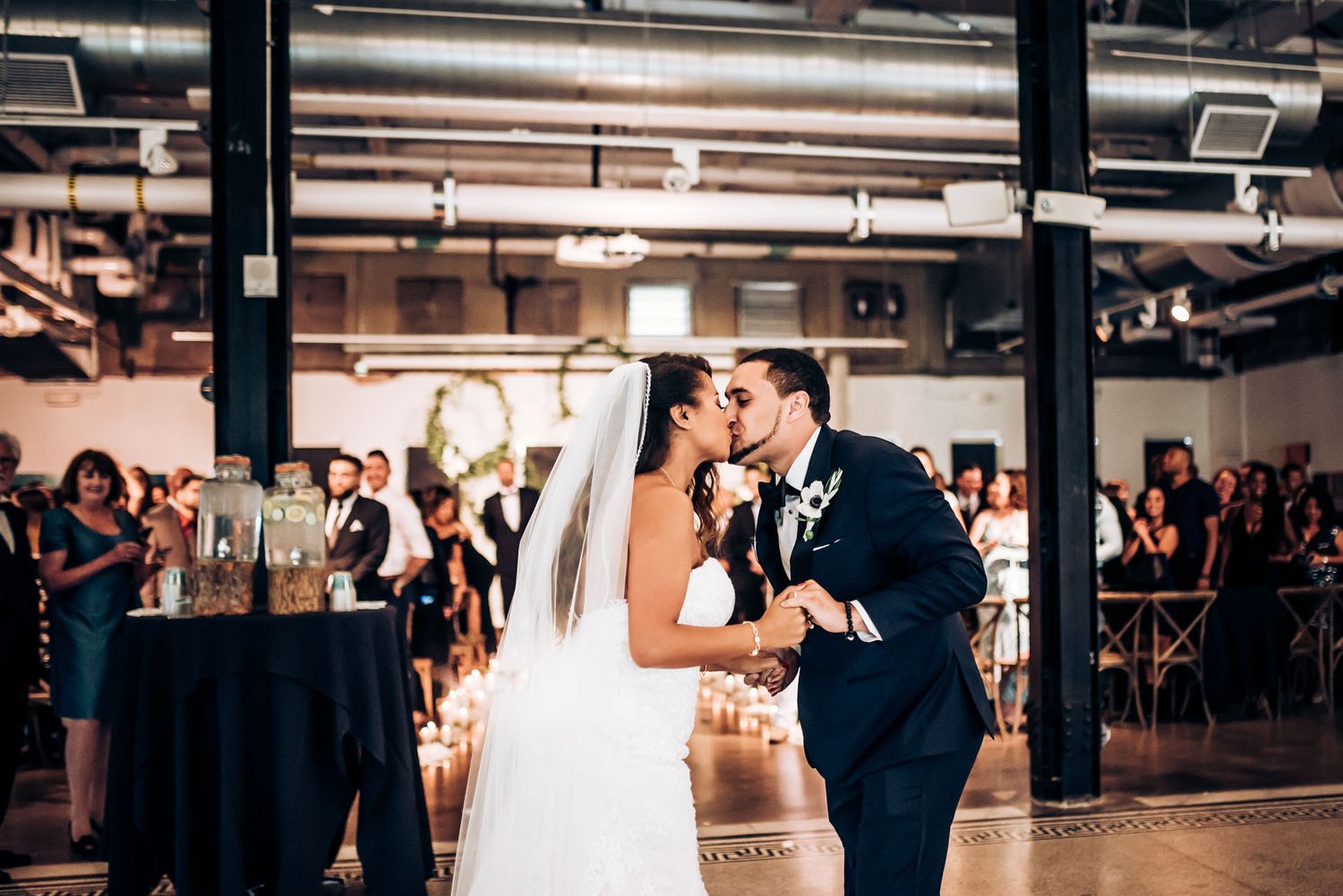 Romantic first kiss moment during wedding ceremony in industrial-style venue.