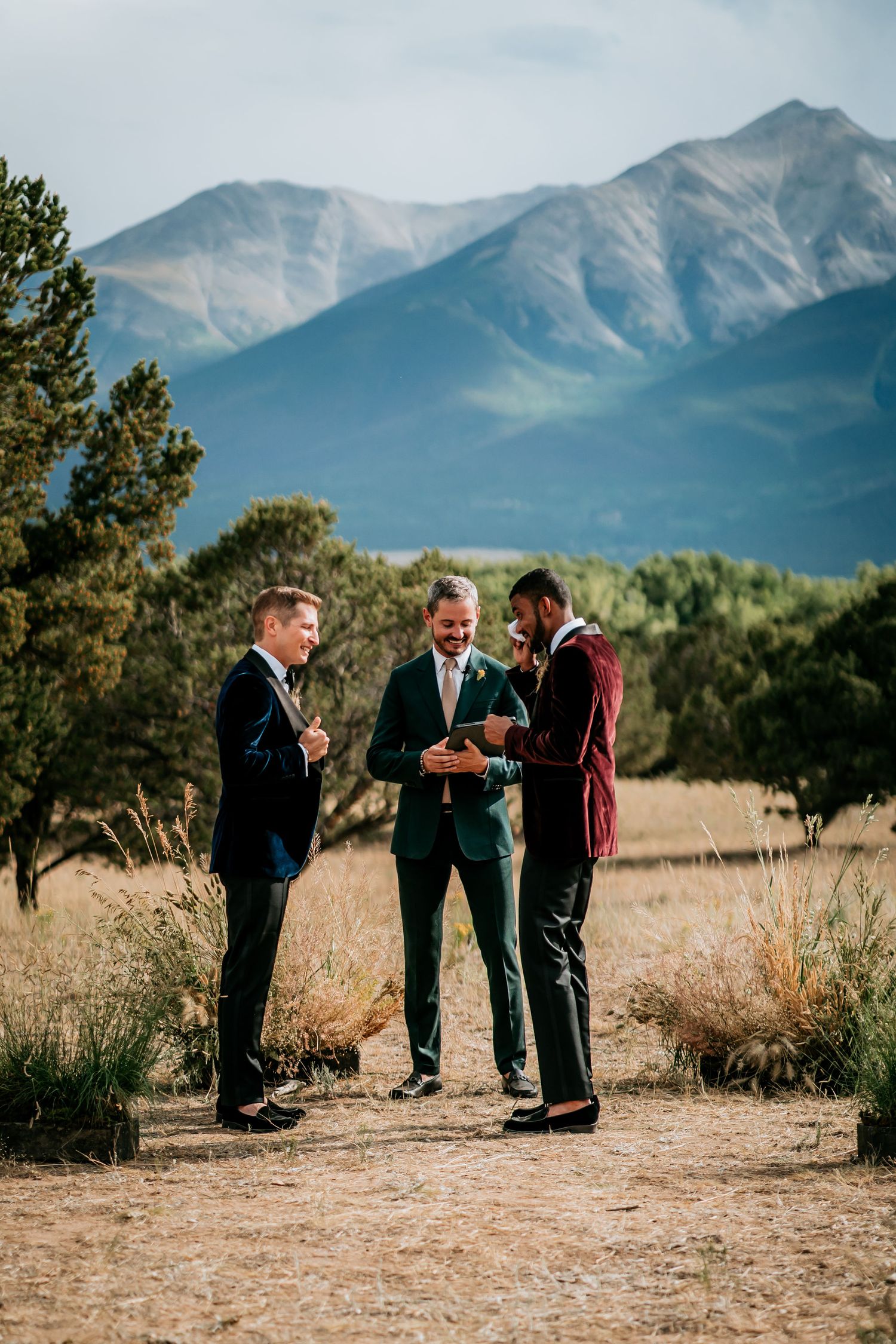 Wedding ceremony participants gathered on a dirt path with towering mountains in the distance.