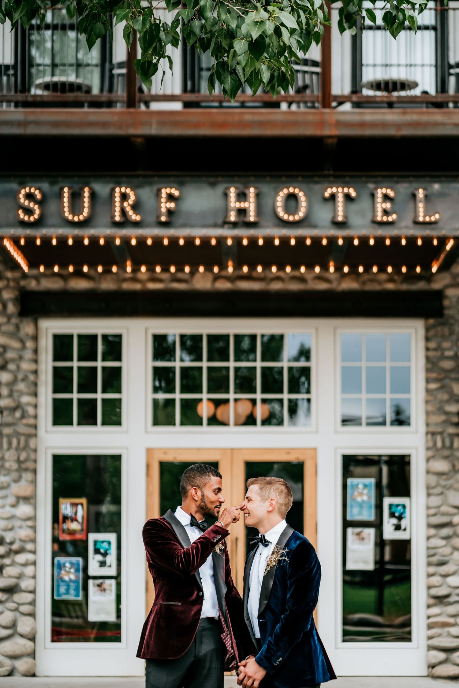 Romantic portrait of couple beneath illuminated Surf Hotel sign at dusk.