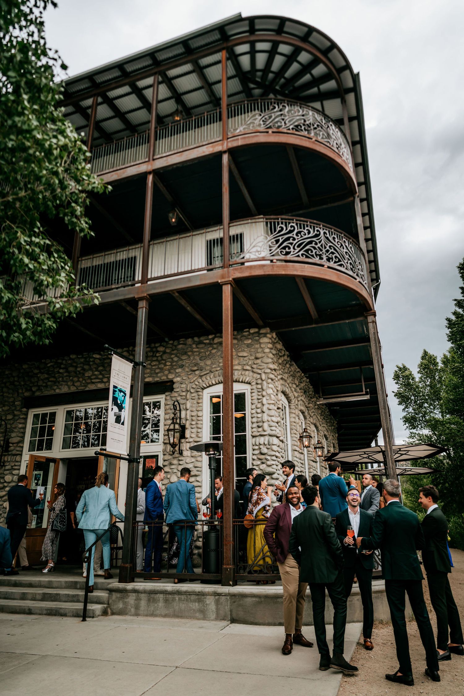 Historic stone building with ornate wraparound balconies filled with wedding guests.
