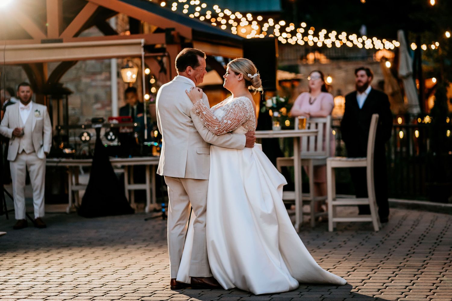 A couple shares their first dance under string lights at an evening wedding reception.