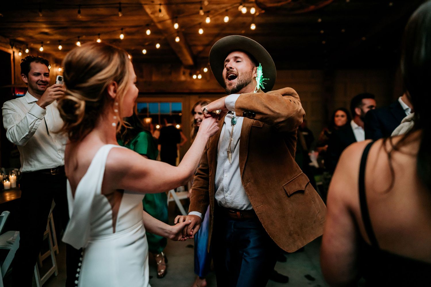 Wedding reception guests dancing energetically under warm indoor lighting at a rustic venue.