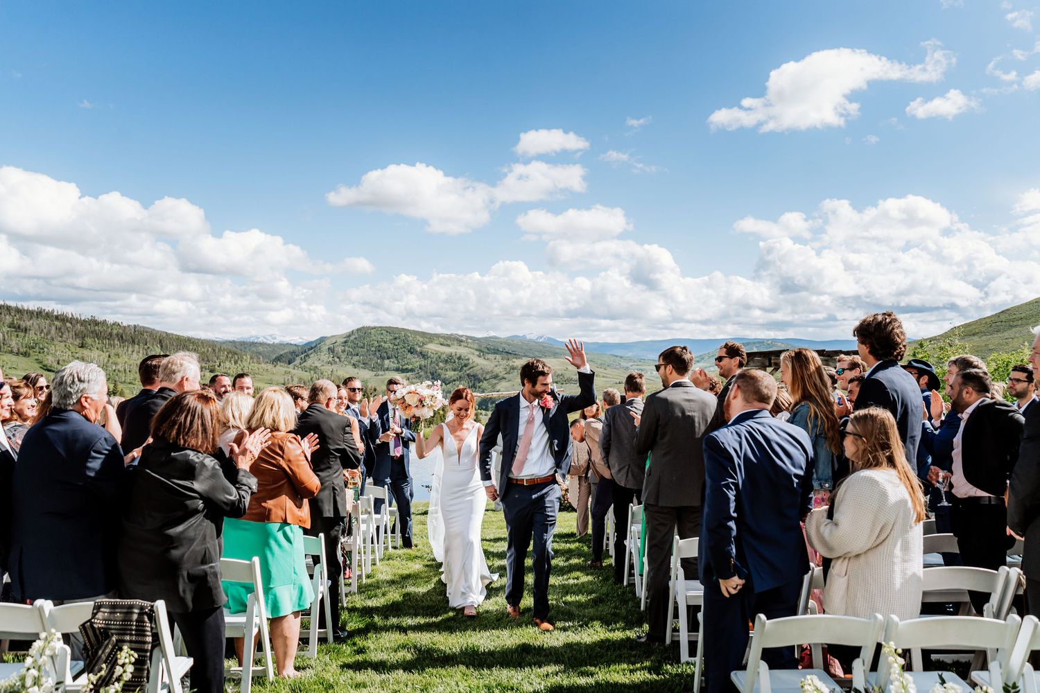 Wedding guests forming aisle for newlyweds exit with mountain scenery in background.