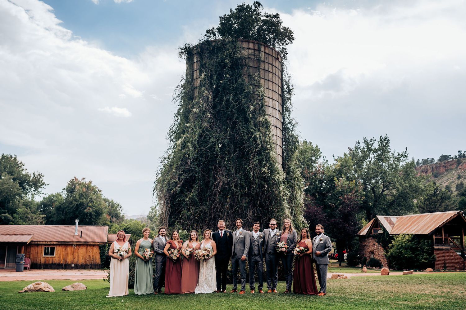 Wedding party poses in front of a unique ivy-covered silo structure on sunny day.
