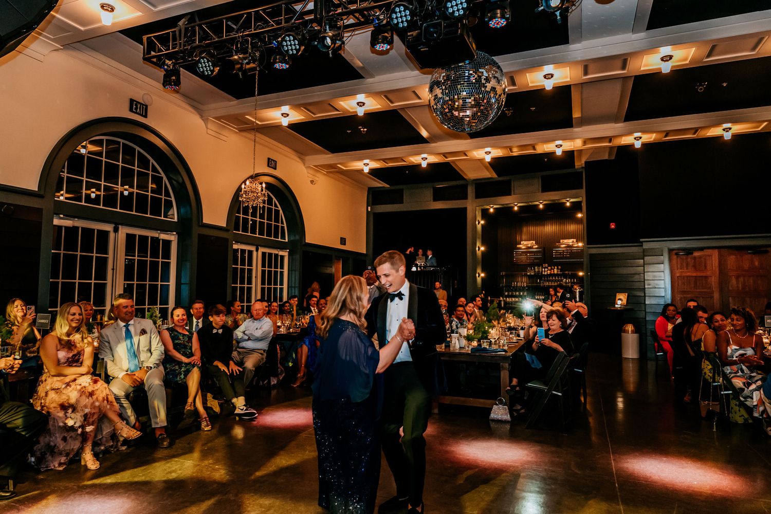 Wedding reception venue with arched windows and disco ball showing couples dancing on the illuminated floor.