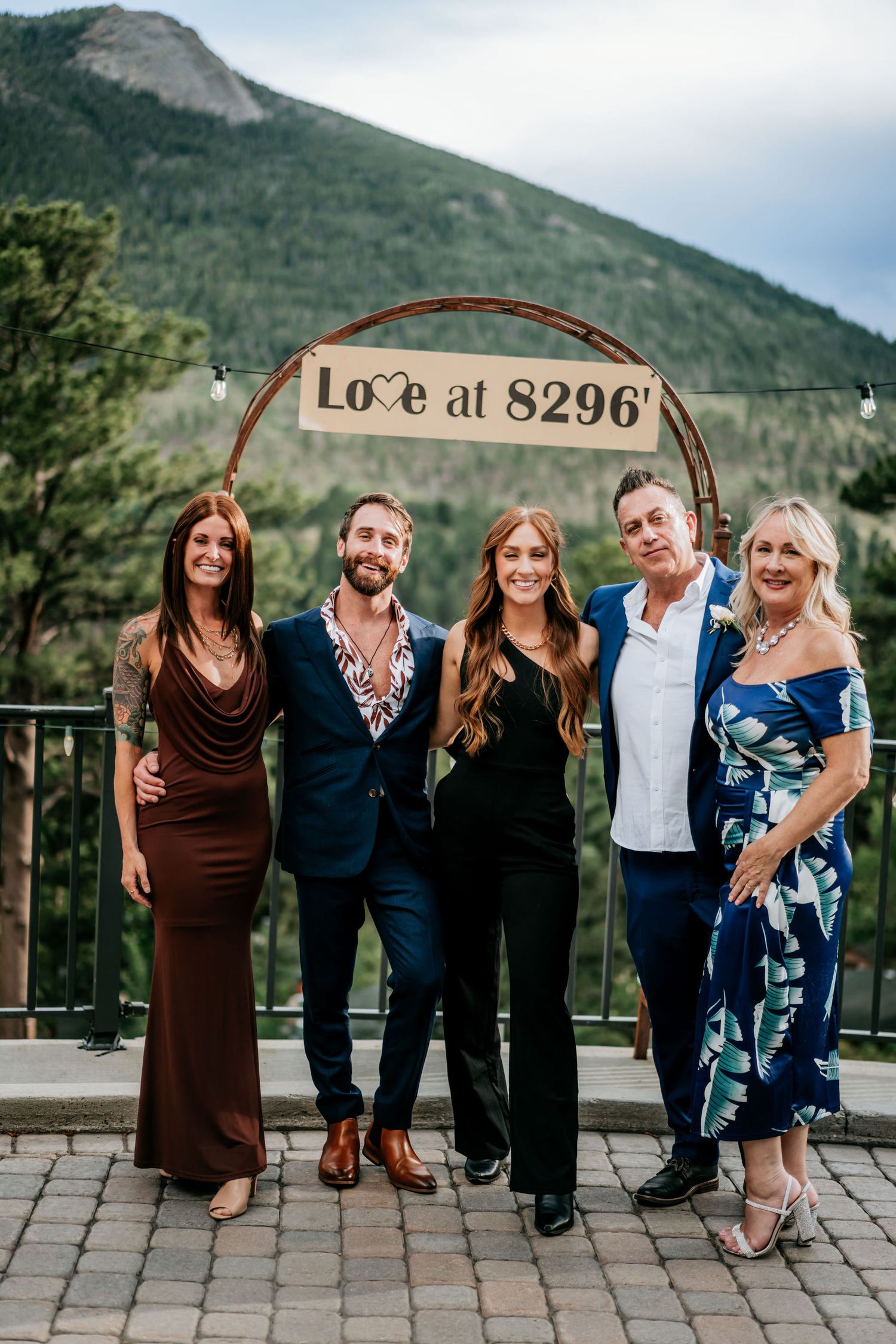 Group portrait beneath a 'Love at 8296' sign with mountain backdrop.