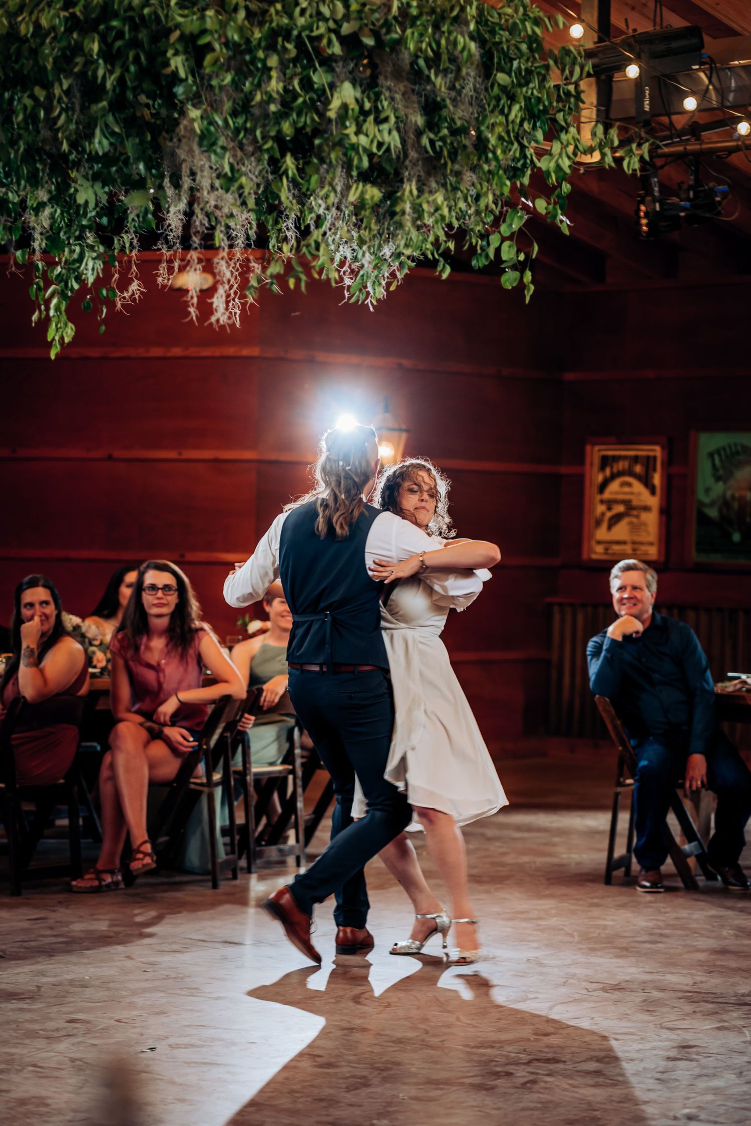 Wedding dancers perform in an indoor venue decorated with hanging plants and mood lighting.