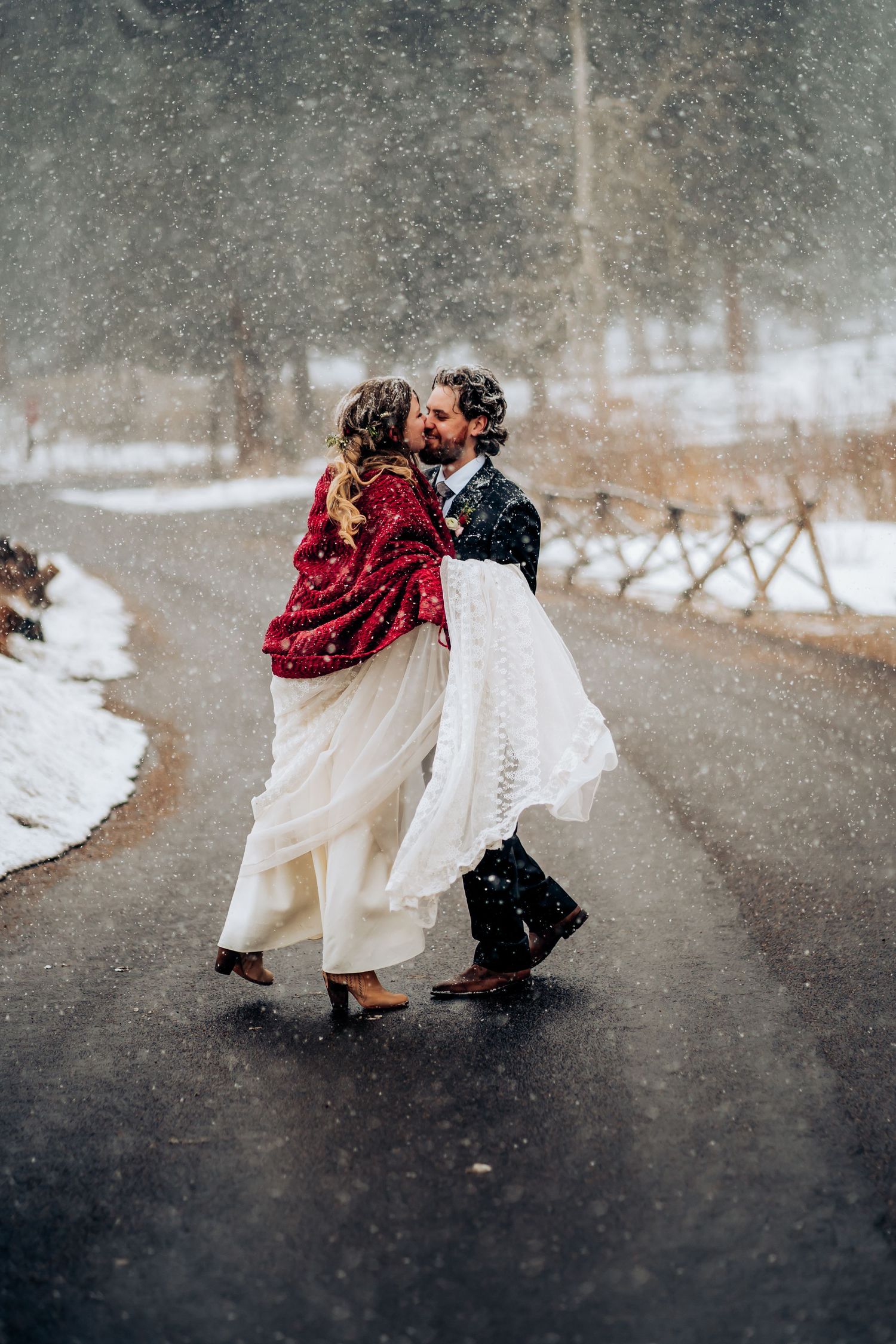 A couple dances in the falling snow, with the bride's white dress and red shawl creating a romantic winter scene.