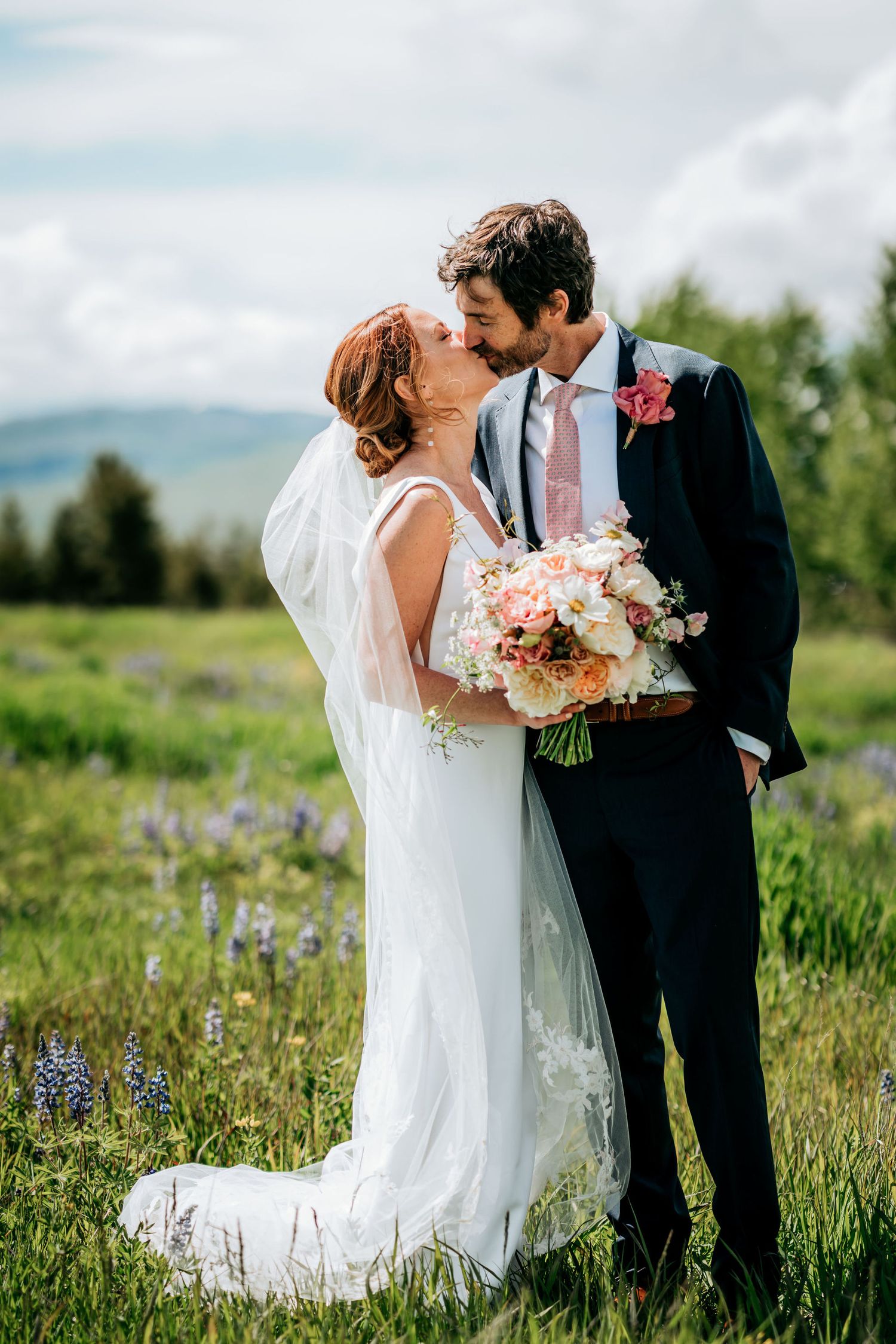 Romantic wedding portrait in a mountain meadow with pink and white bouquet.