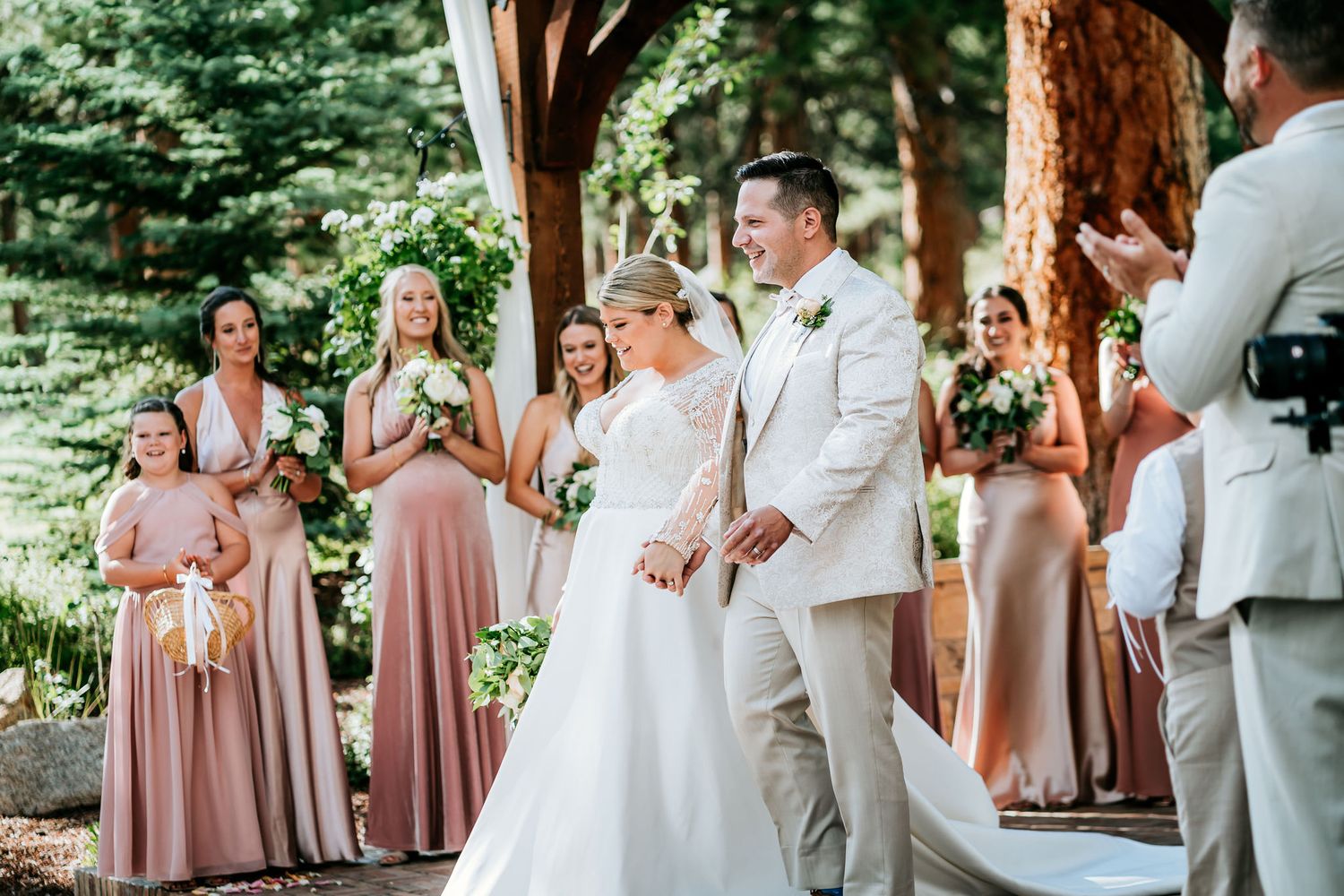 Wedding ceremony taking place under wooden beams with attendants in pink dresses.