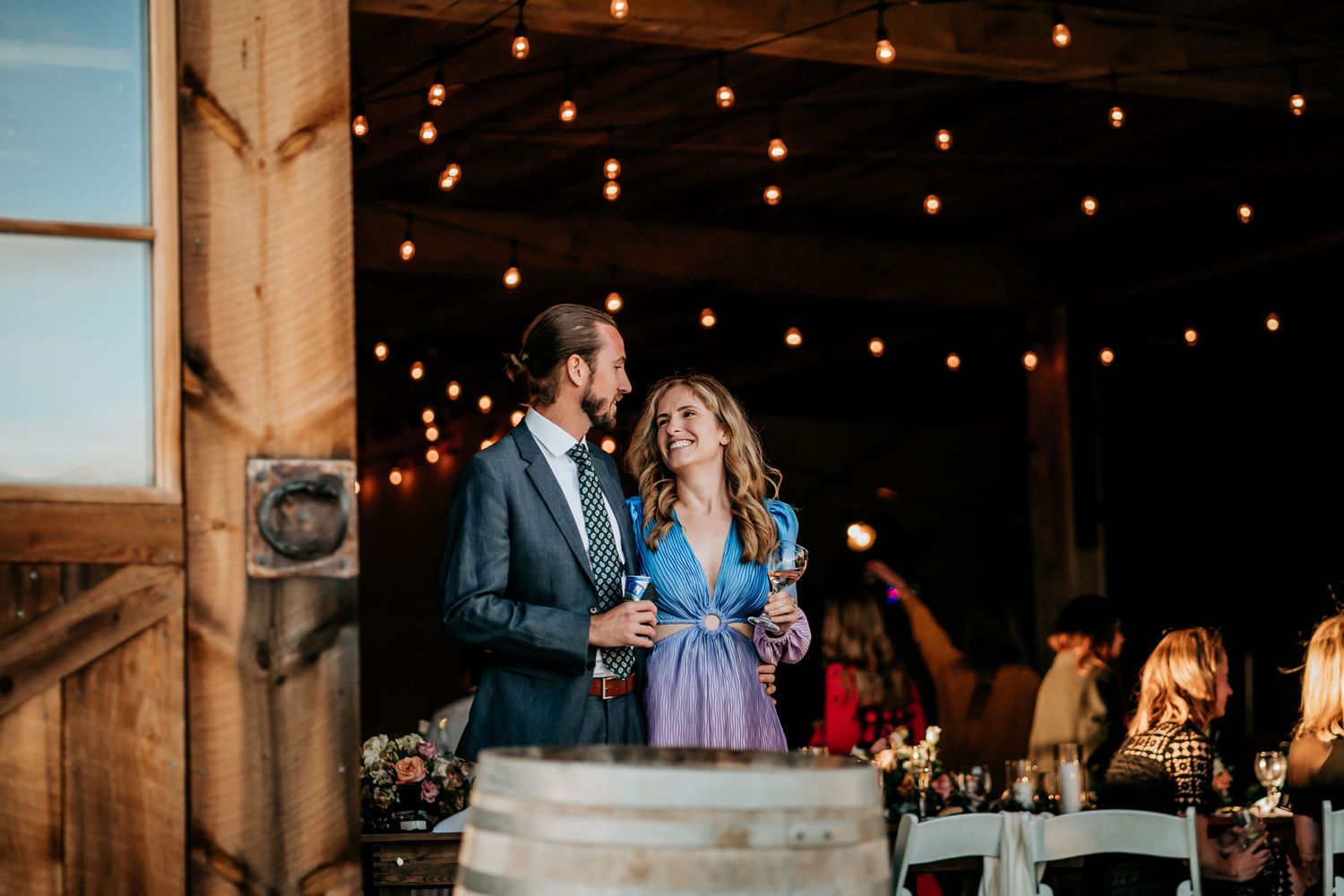 Couple shares intimate moment under twinkling string lights at rustic barn reception.