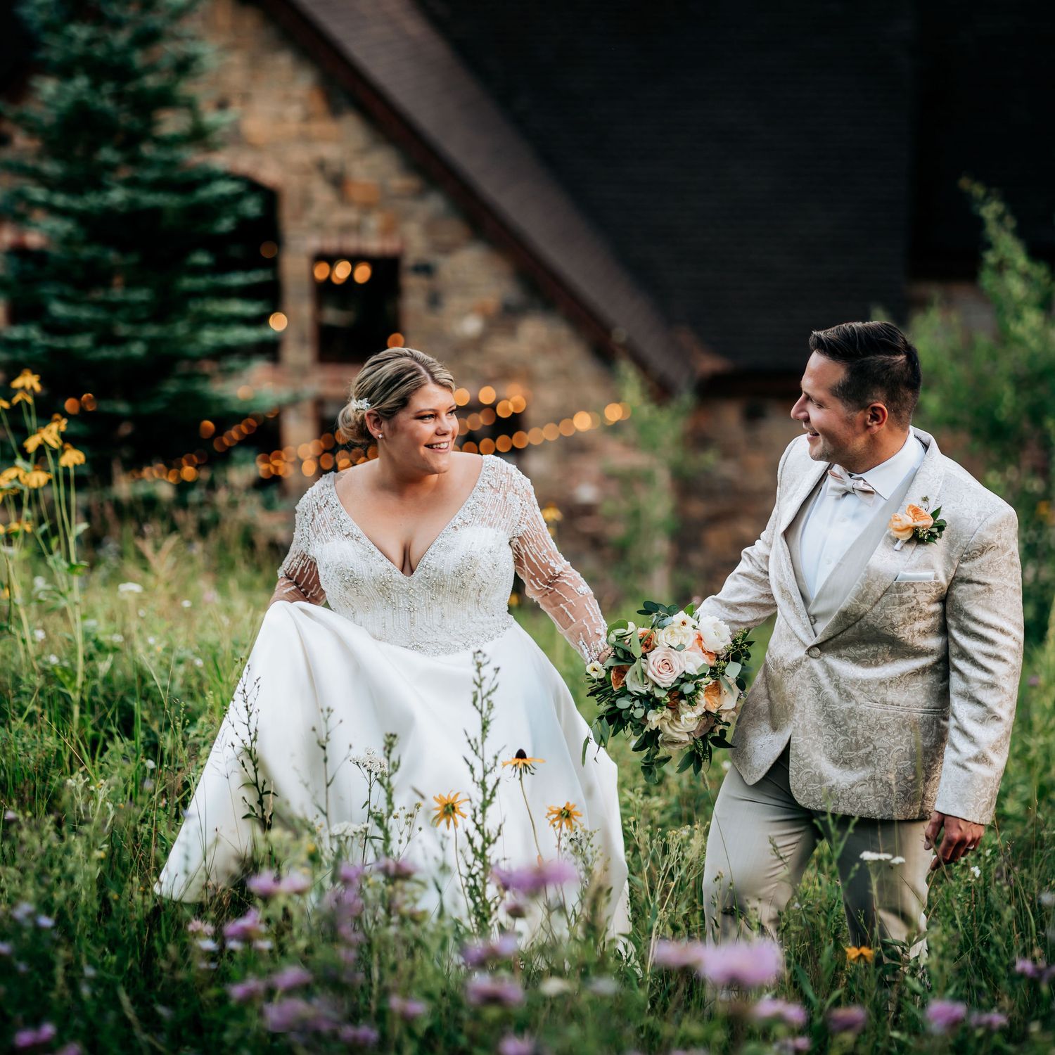 Wedding couple walking through wildflowers near rustic venue.